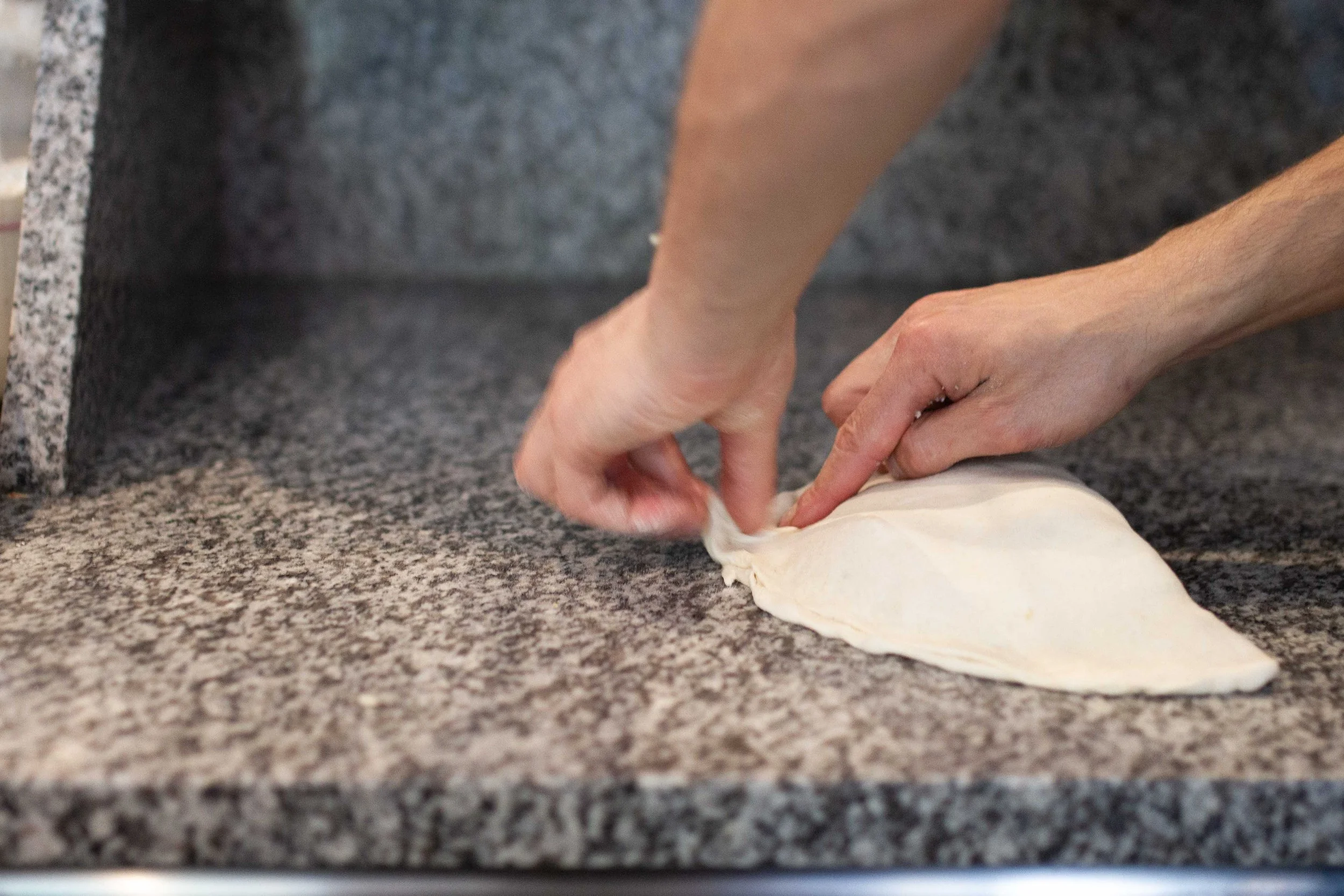 Person folding dough on a speckled gray granite countertop.
