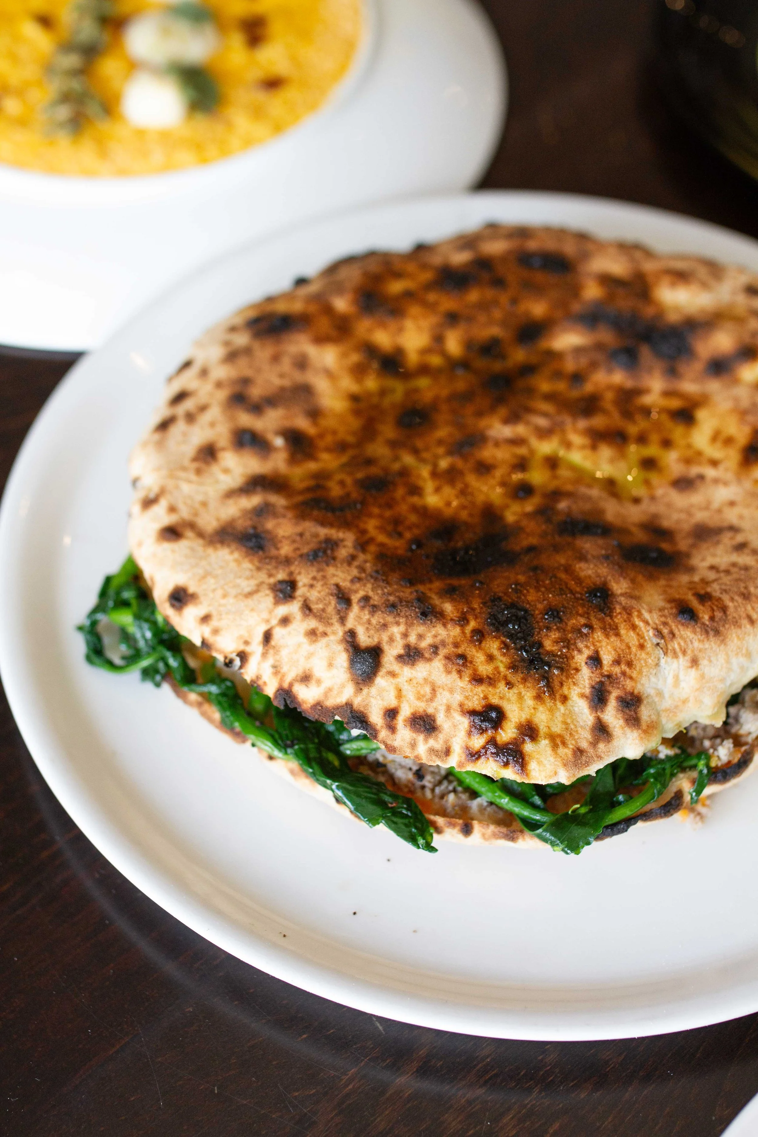 Close-up of a toasted naan bread sandwich filled with spinach and ground meat on a white plate
