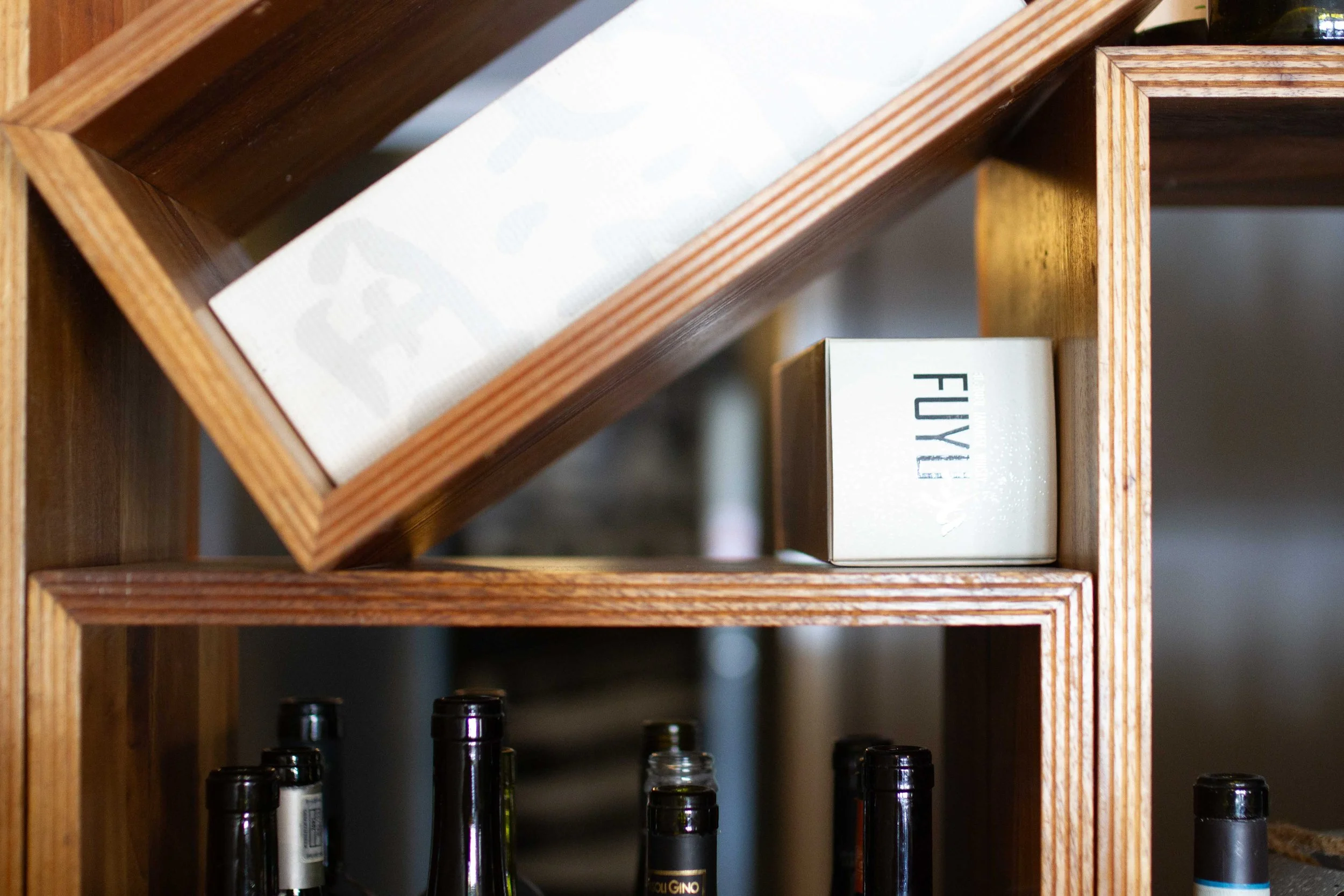 Wooden wine rack with bottles on the bottom shelf and a box labeled 'FUKY' on the middle shelf.