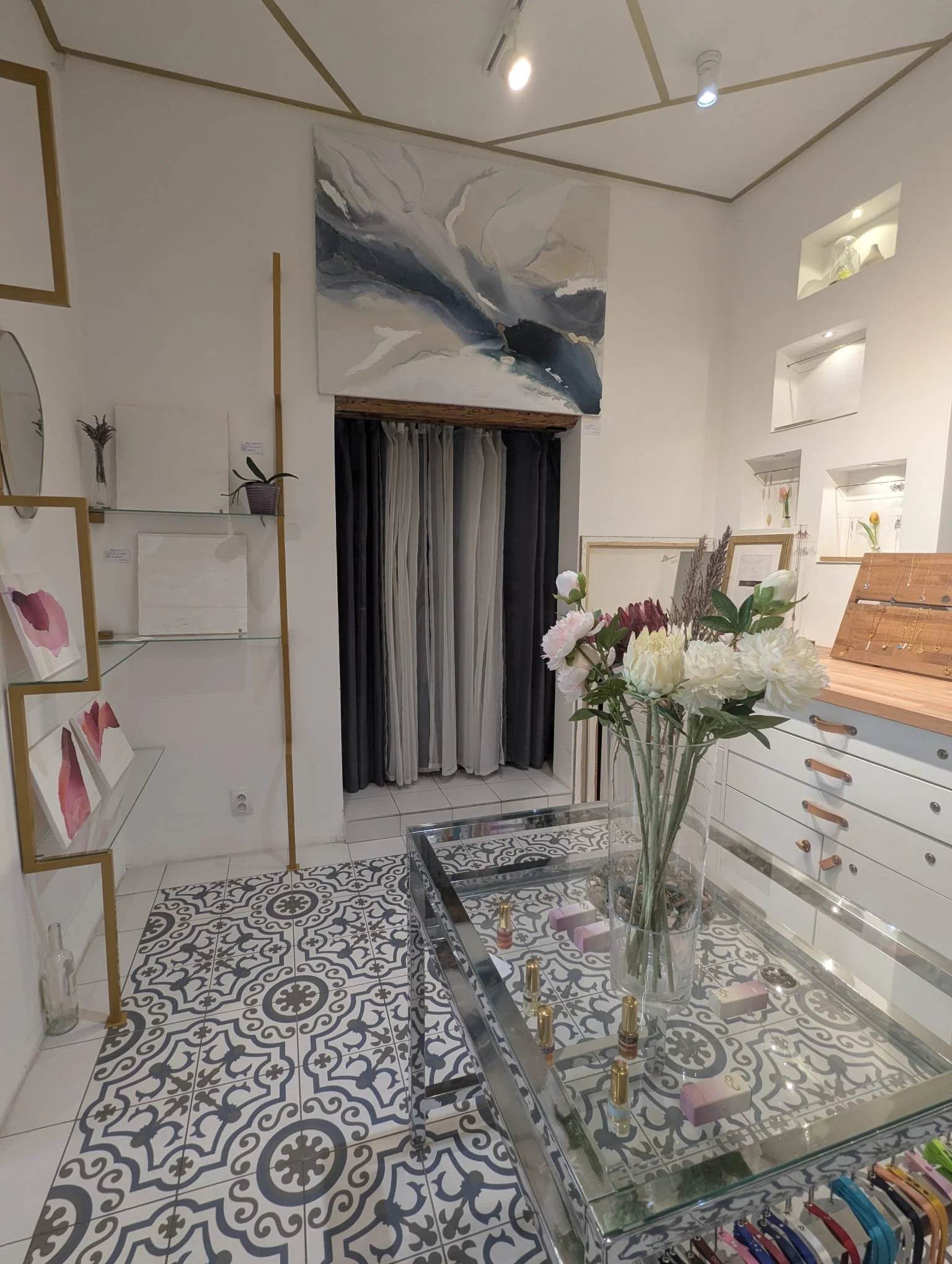 Interior of a boutique and art gallery with decorative shelving with artwork, a large floral arrangement on glass table, and artwork on the walls.