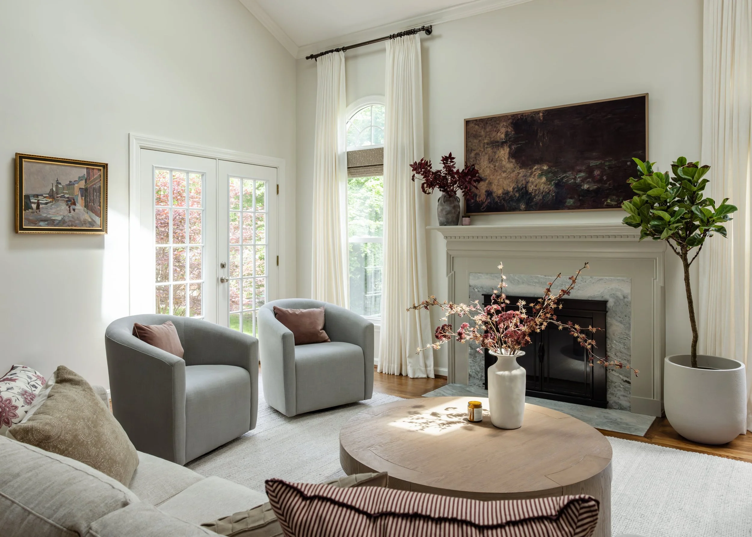 Bright living room with large windows, white walls, a fireplace, and decorative plants.