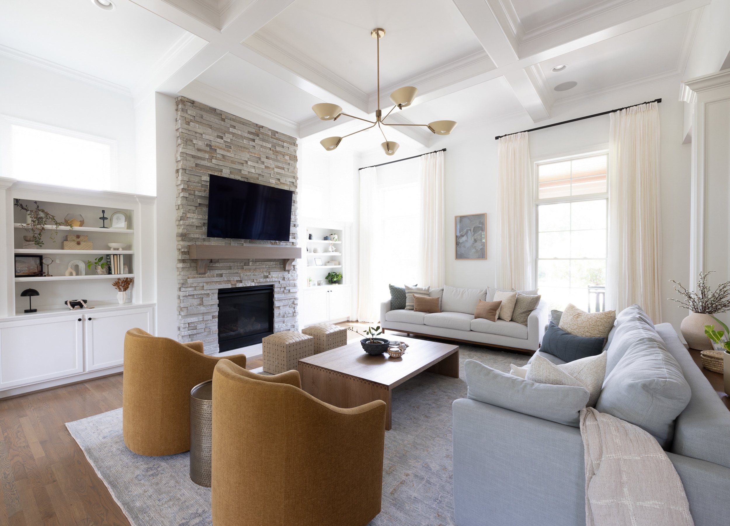 Bright living room with stone fireplace, white sofa and modern chandelier.
