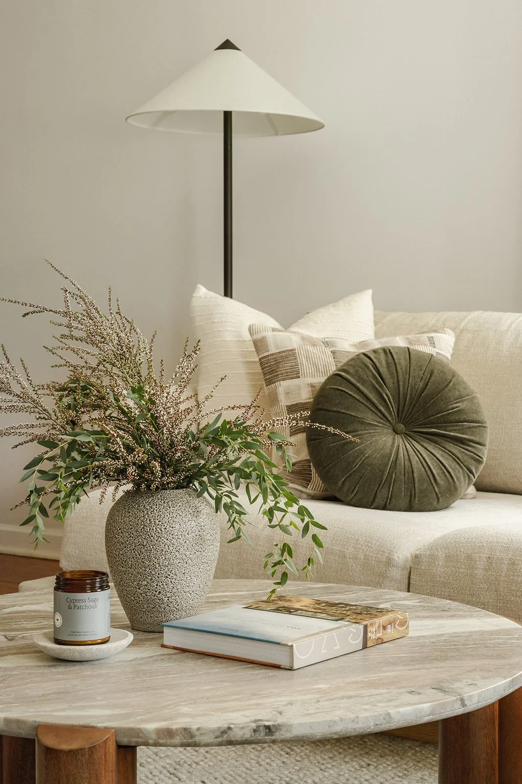 Neutral living room with layered pillows, floor lamp and styled coffee table with greenery.