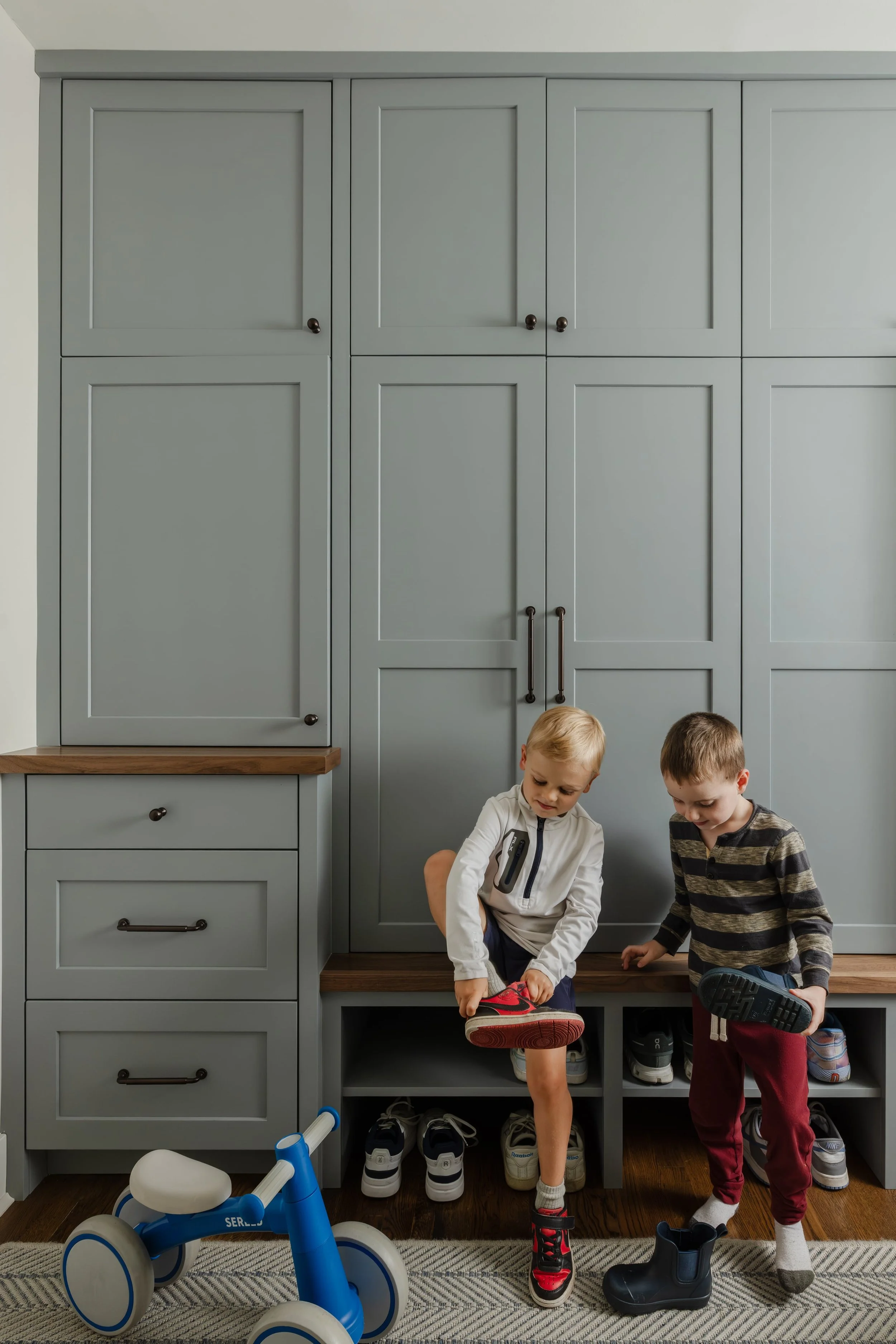 Two children putting on shoes beside custom mudroom storage.