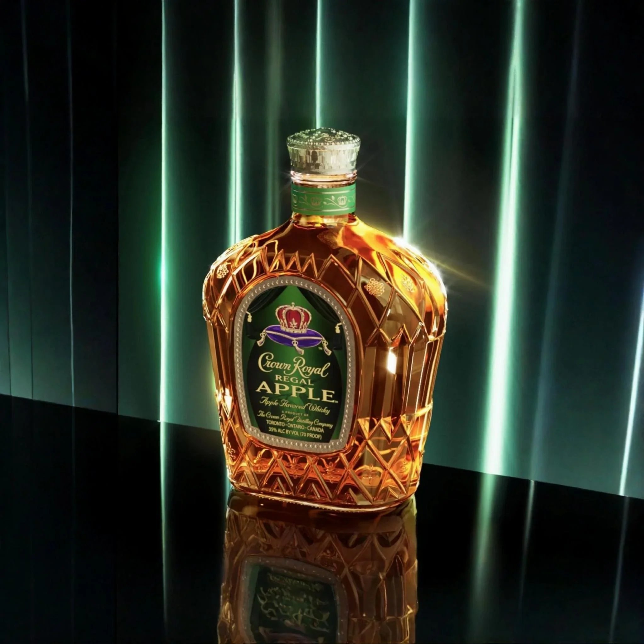 A decorative glass bottle of Crown Royal Regal Apple whiskey with a green label, gold accents, and a crown logo, placed on a reflective black surface with vertical green and white light streaks in the background.