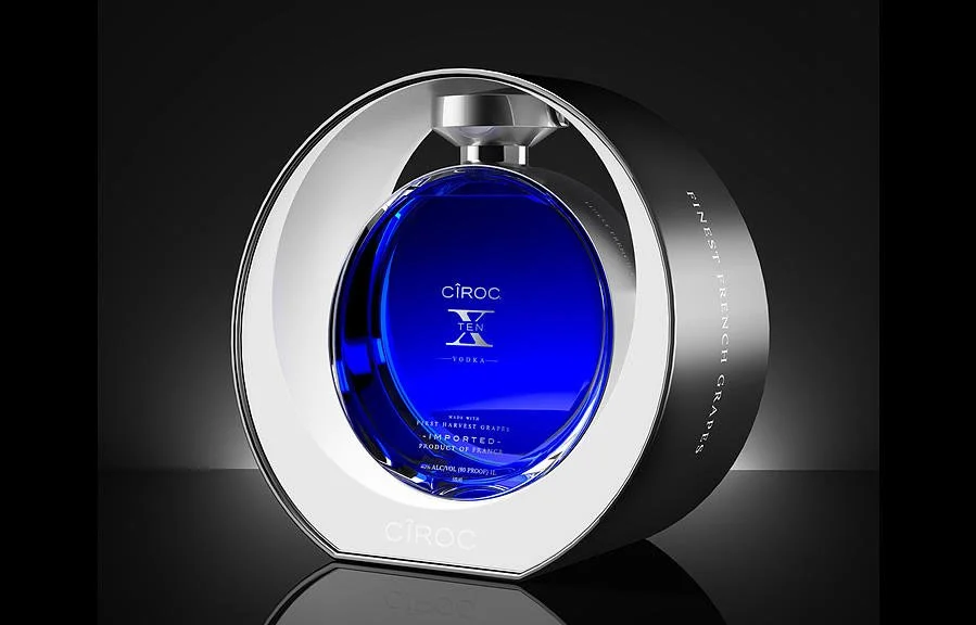A blue bottle of Ciroc TEN vodka inside a modern circular display with silver and black accents.