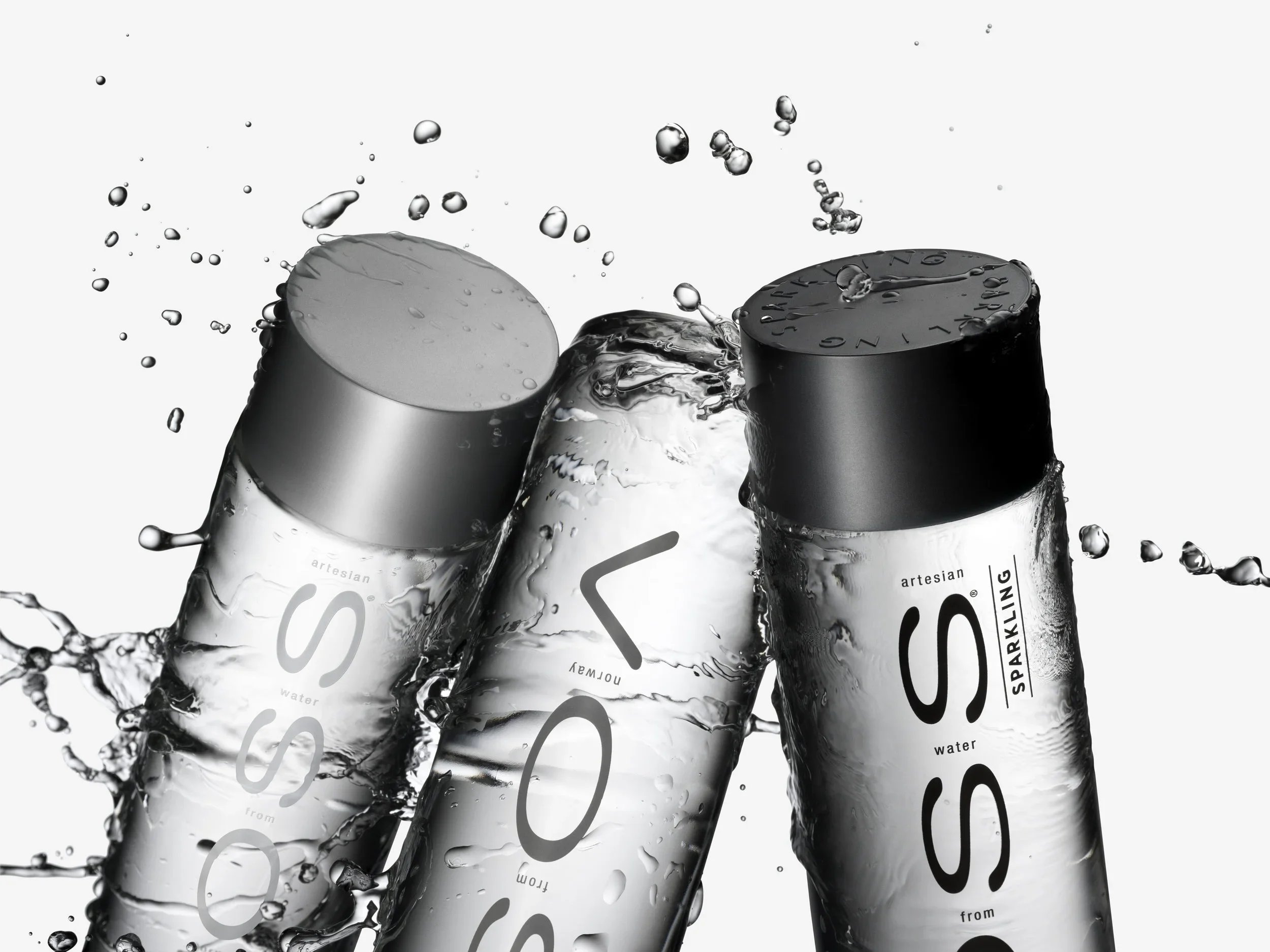 Three bottles of VOSS water splashing with water droplets in midair.