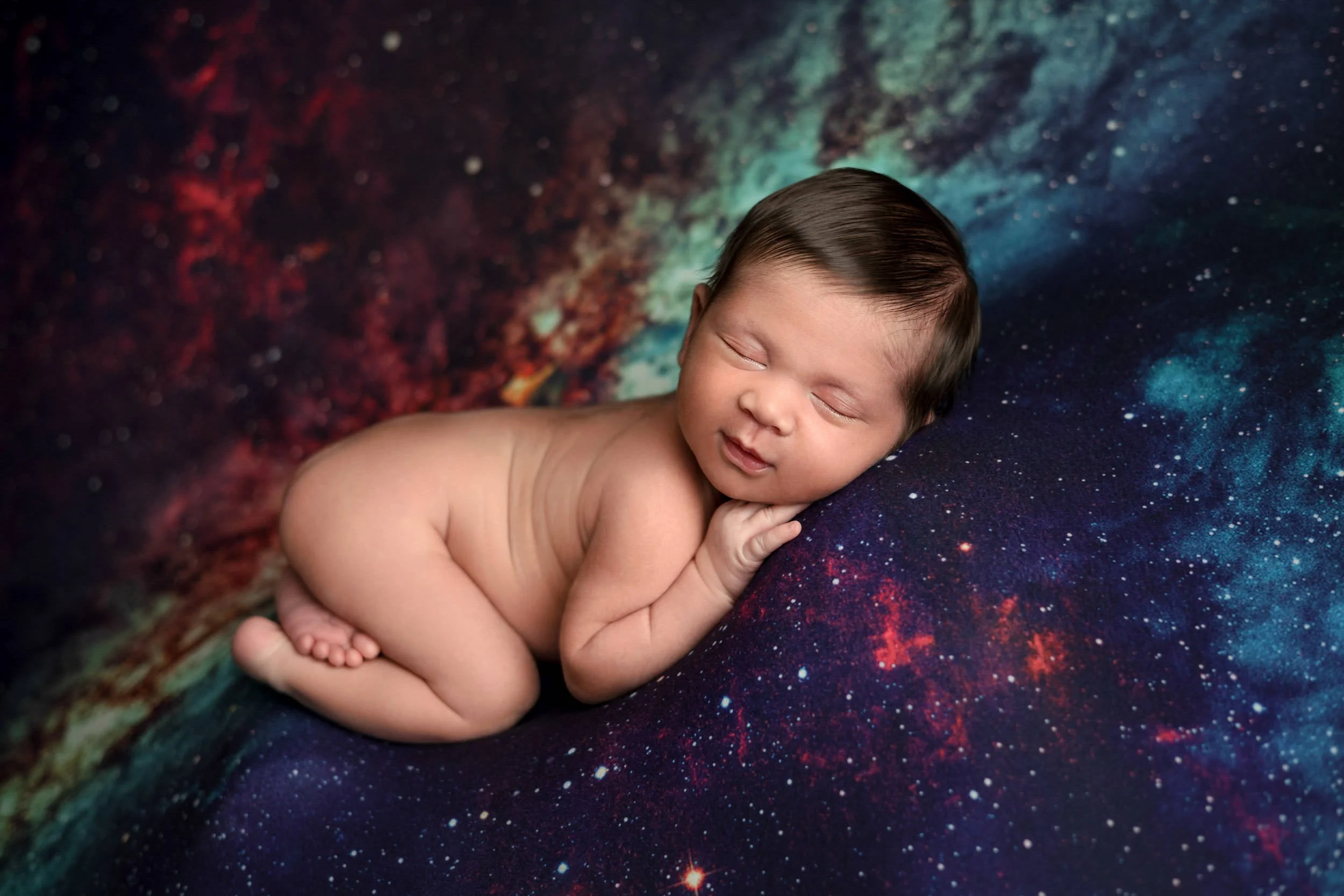 Newborn baby sleeping on a galaxy-patterned blanket.