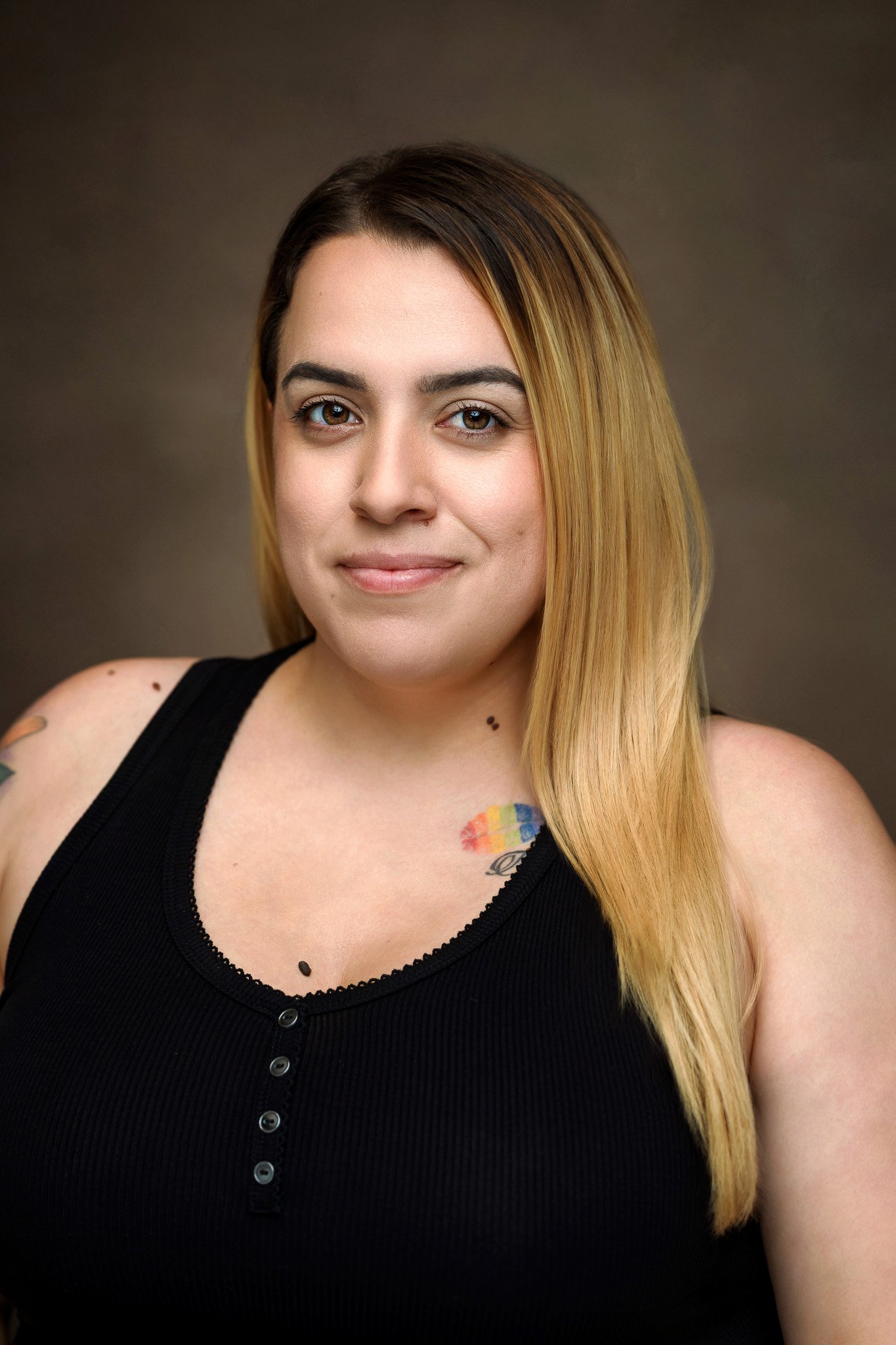 Portrait of a woman with long, straight blonde hair, wearing a black sleeveless top, against a neutral background.