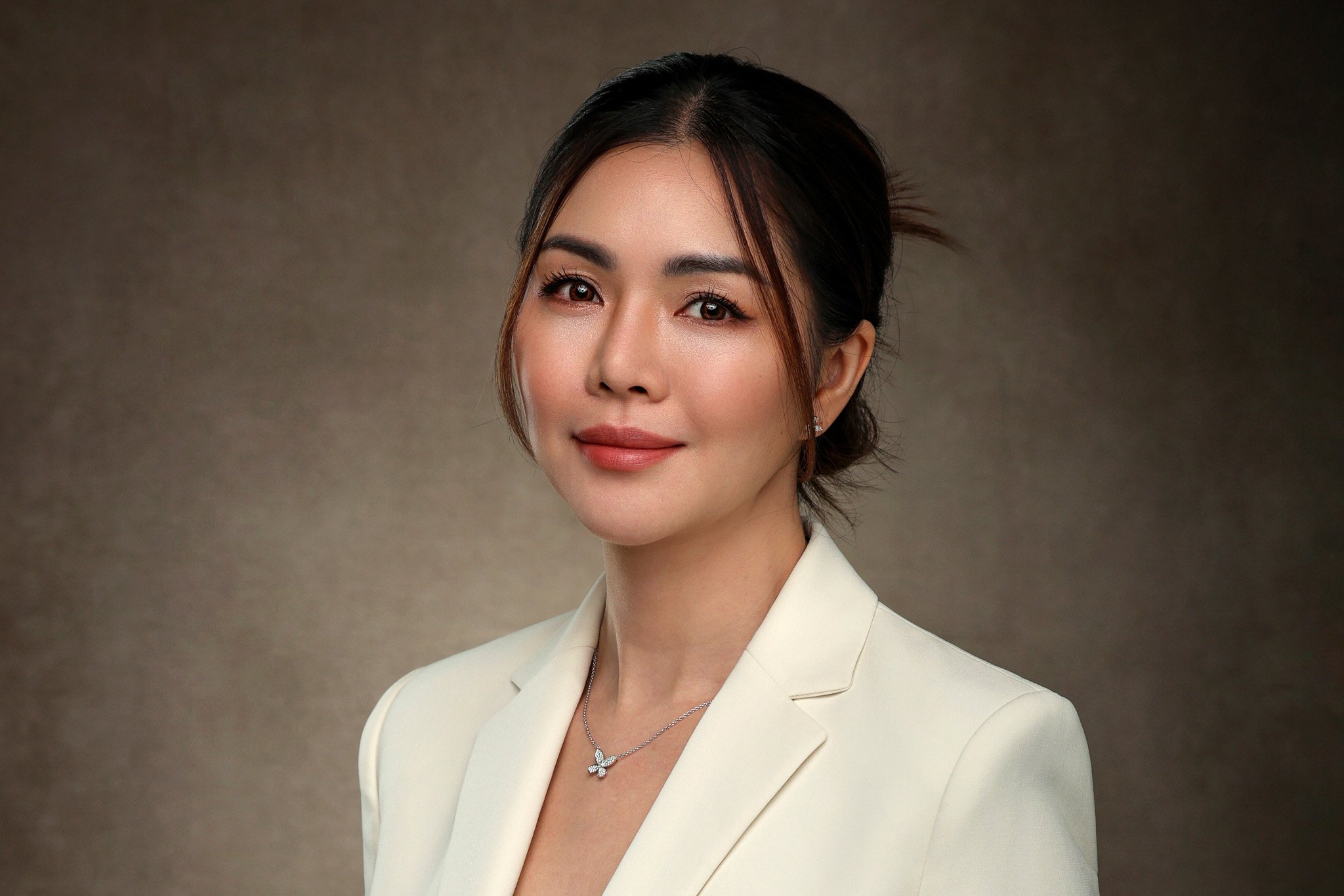 Portrait of a woman with short dark hair, wearing a white blazer and a butterfly pendant necklace, against a plain background.