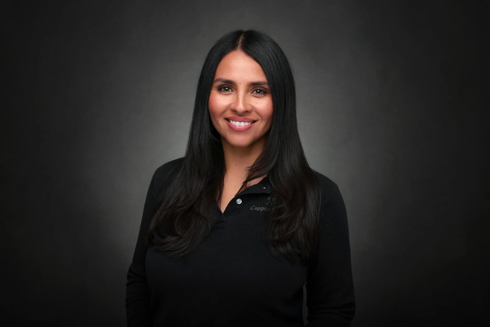 Portrait of a woman with long black hair wearing a black top against a dark background.