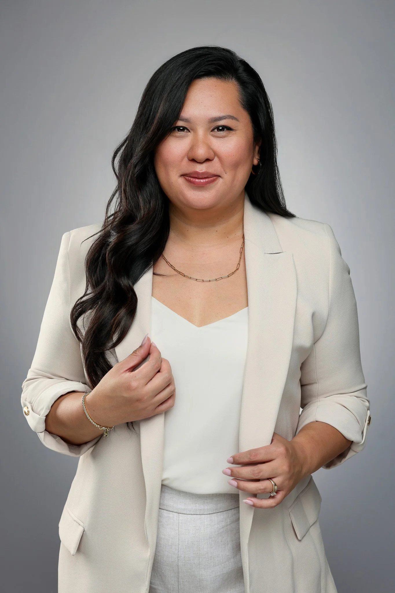 A woman in a cream-colored suit with long, wavy dark hair, posing against a neutral background.