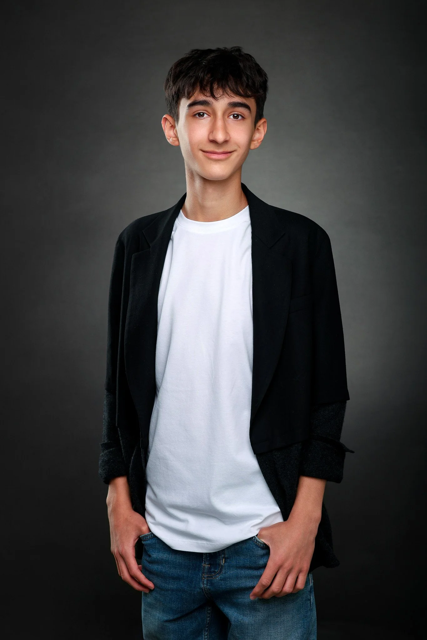 Smiling young man in casual attire standing against a dark background.