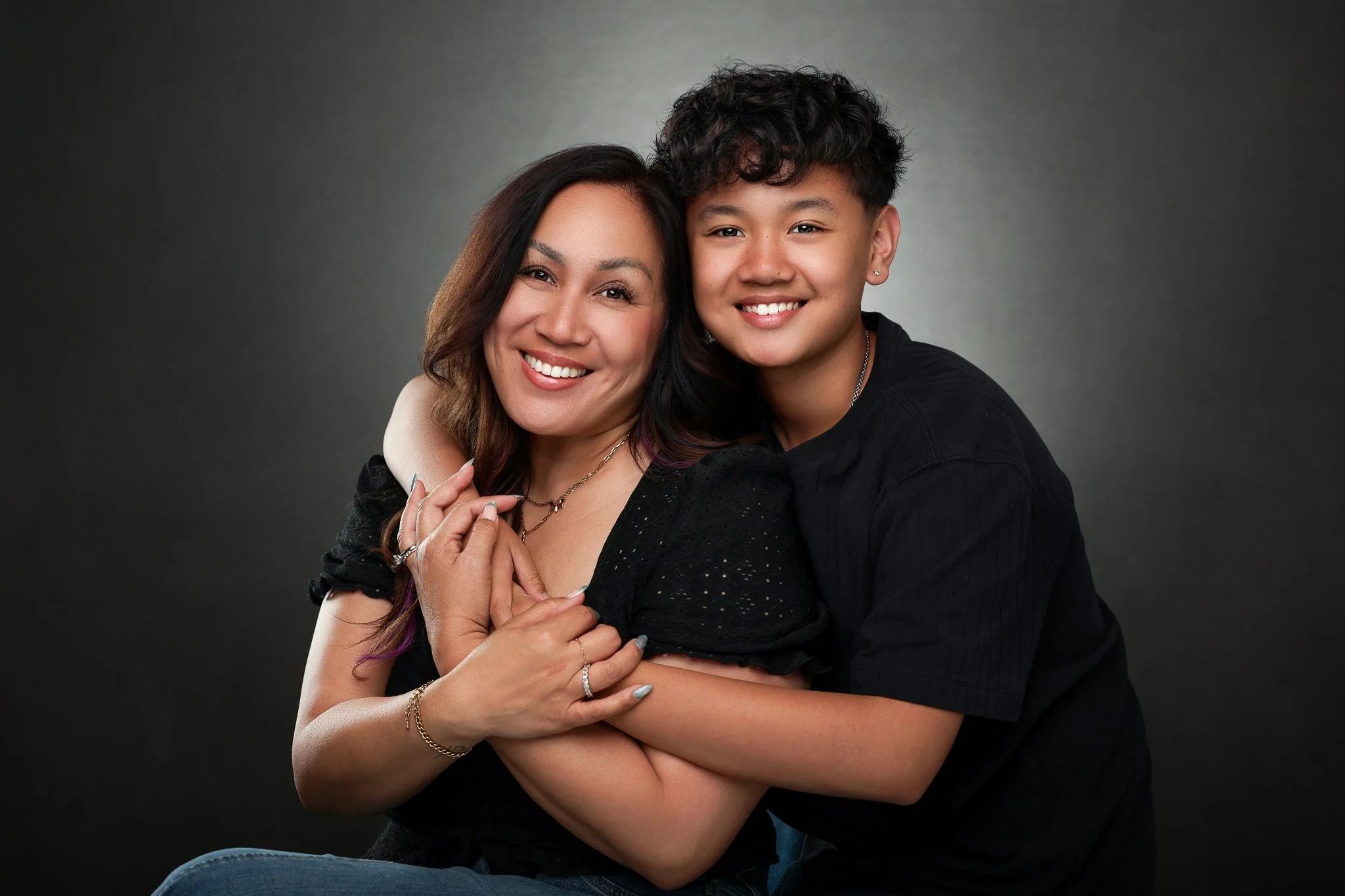 A smiling woman and a young girl hugging against a gray background.