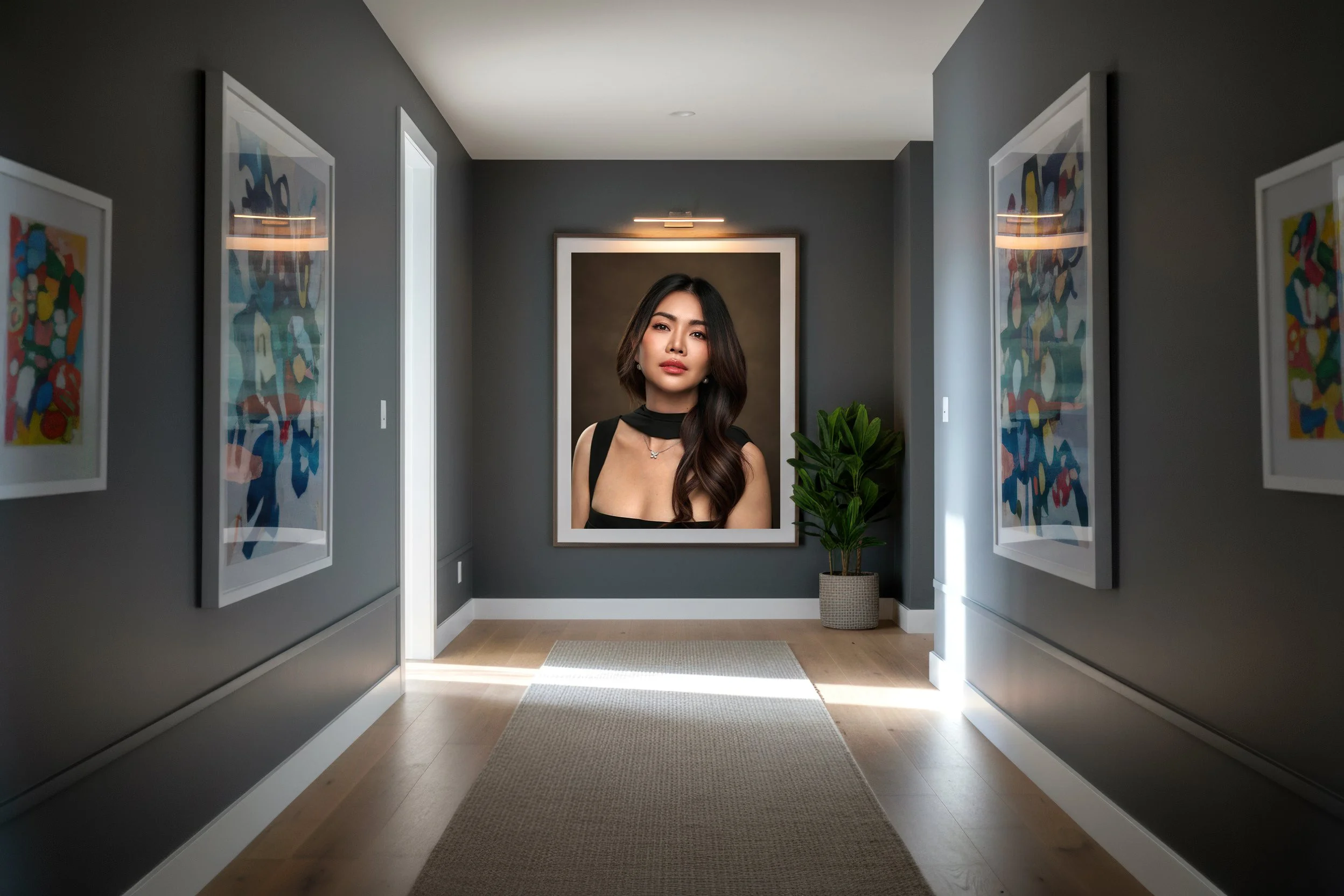 A woman with long, dark hair, wearing a black sleeveless top and a necklace, stands in an art gallery corridor with dark gray walls. The corridor is painted with colorful abstract art, and a potted plant is situated on the right side. A large framed portrait of the woman is on the wall behind her.
