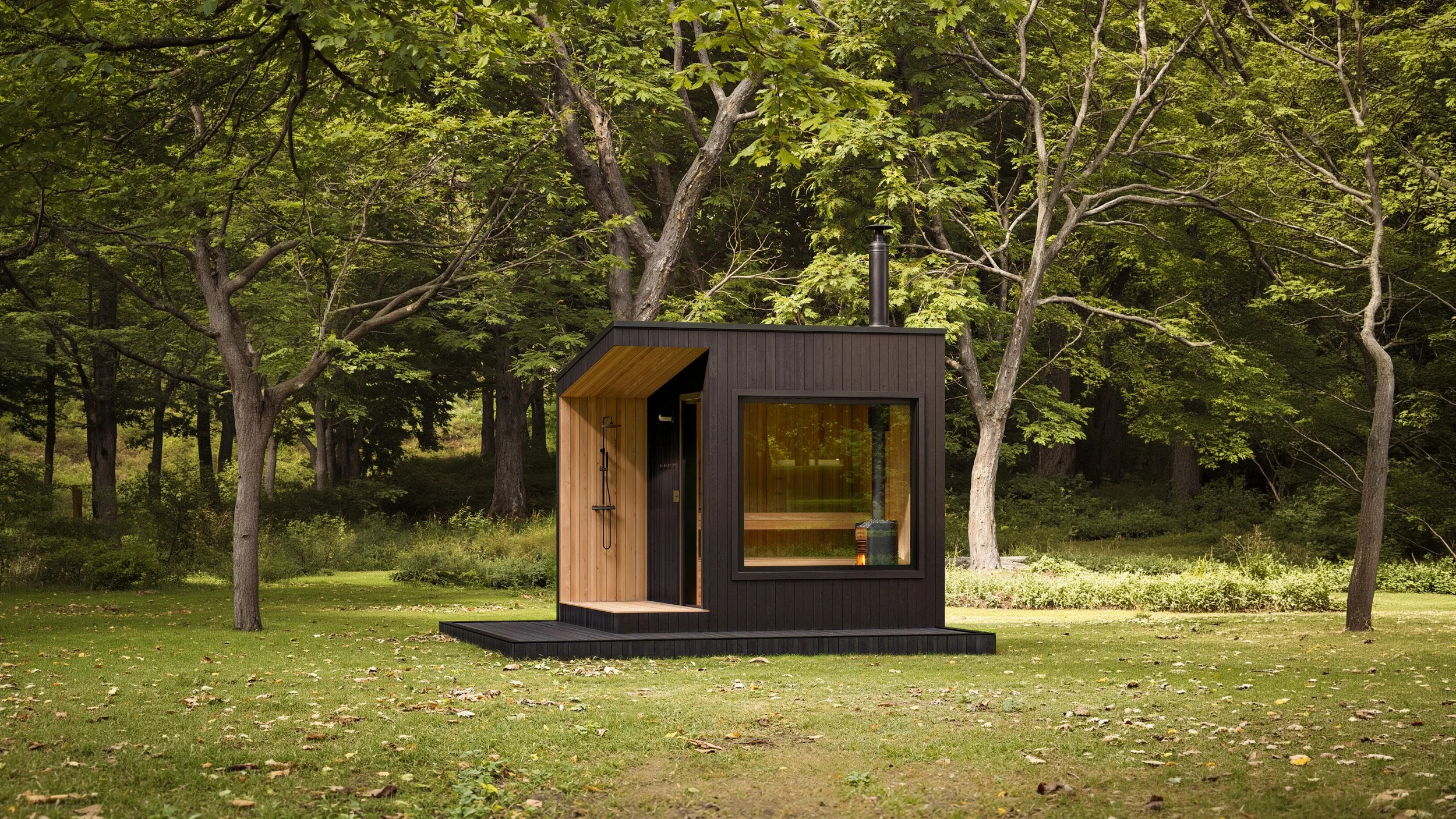 A small black and wood-paneled modern cabin with a large glass window and an outdoor shower, situated in a lush green forest clearing.