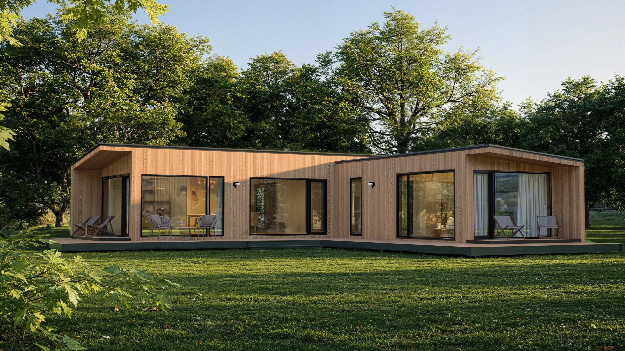 Modern wooden house with large glass windows and sliding doors, situated on a grassy lawn with tall green trees in the background.