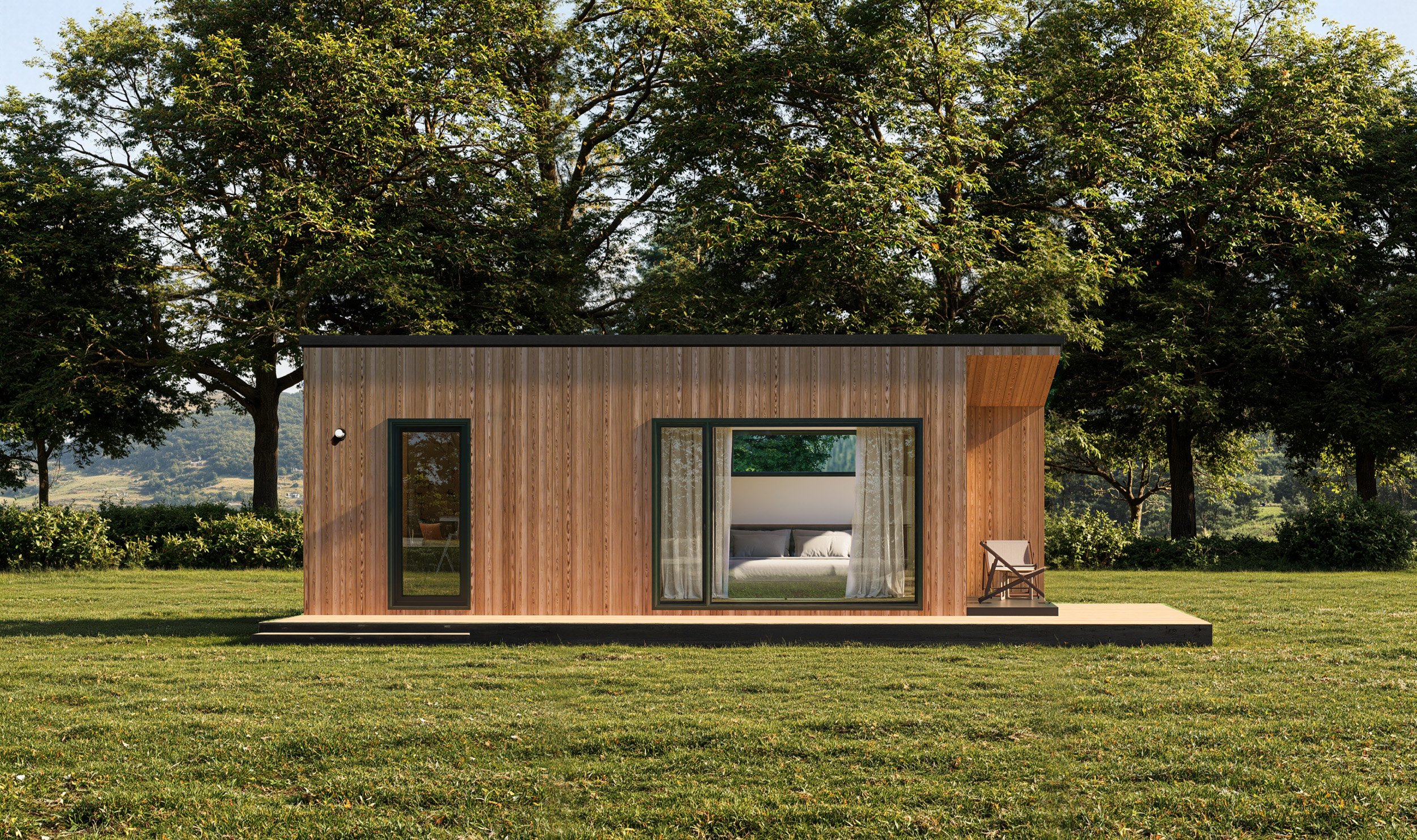 Small modern wooden house with large window and door, surrounded by greenery, on a grassy lawn with trees in the background.