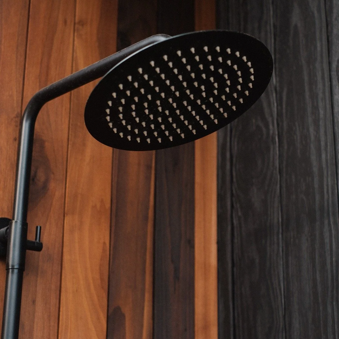 Close-up of a black rainfall shower head mounted to a wall with wood paneling.