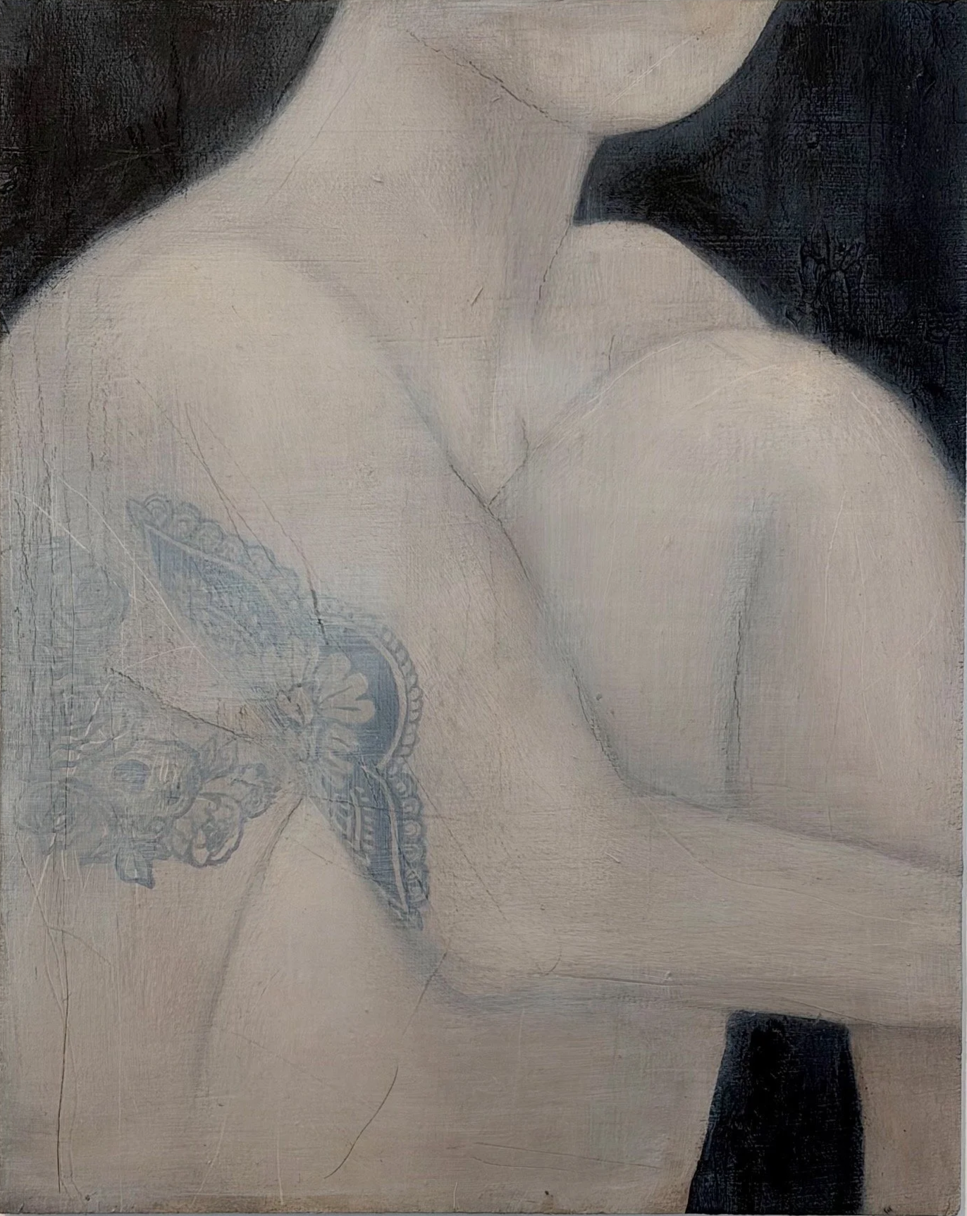 Close-up view of a woman's nude shoulder and neck, revealing a blue tattoo on her upper chest.