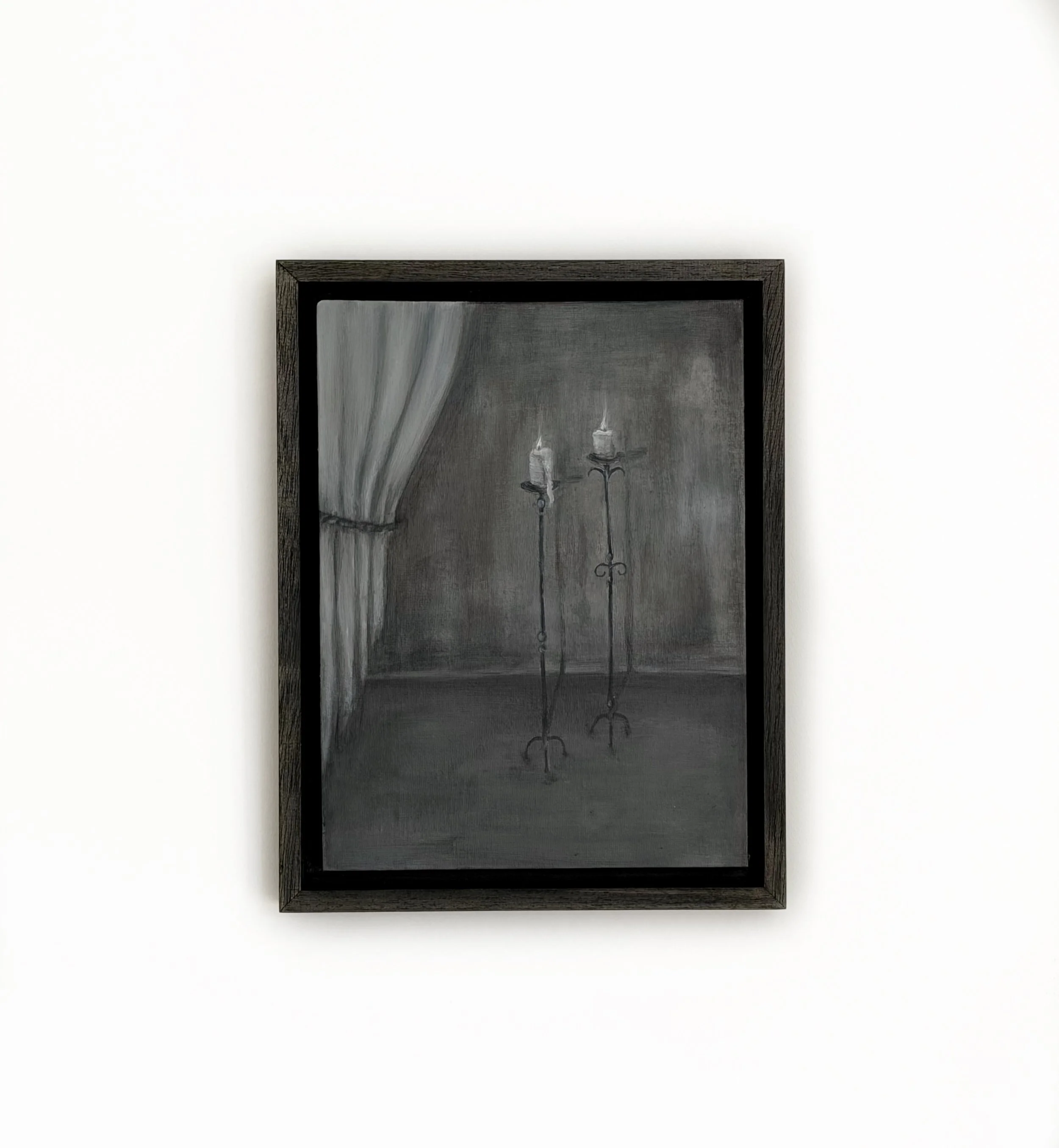 A black framed picture on a white wall depicting two lit candles and a white curtain.