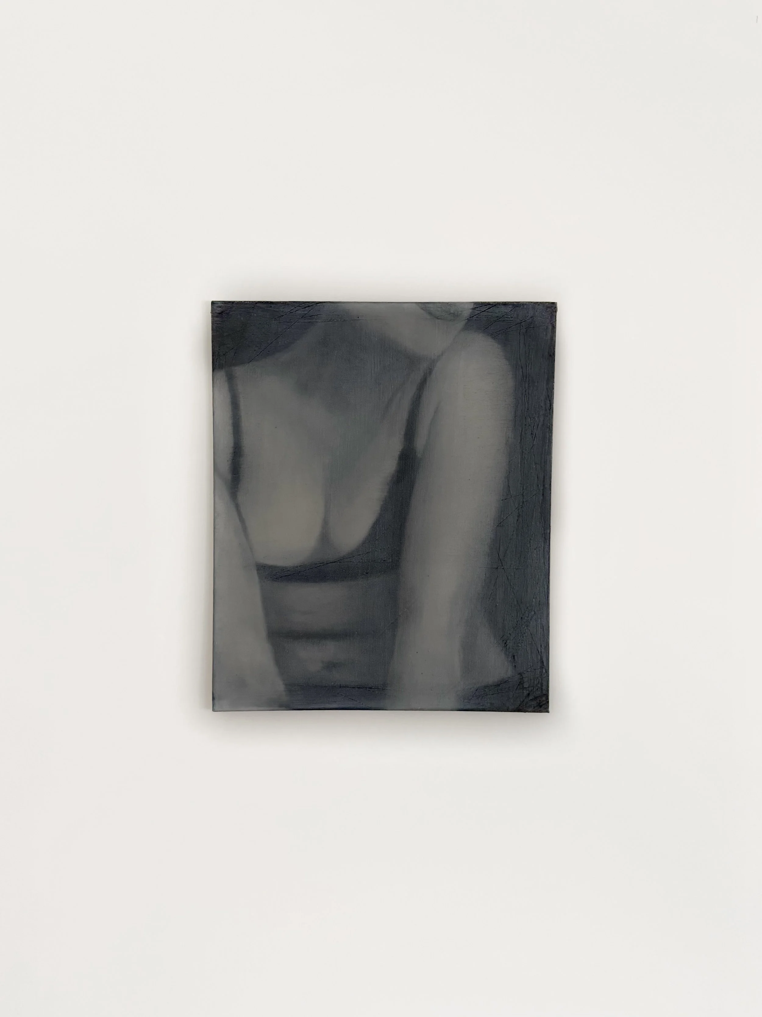 A black and white photograph of a human figure reflected on a shiny, dark surface, mounted on a white wall.