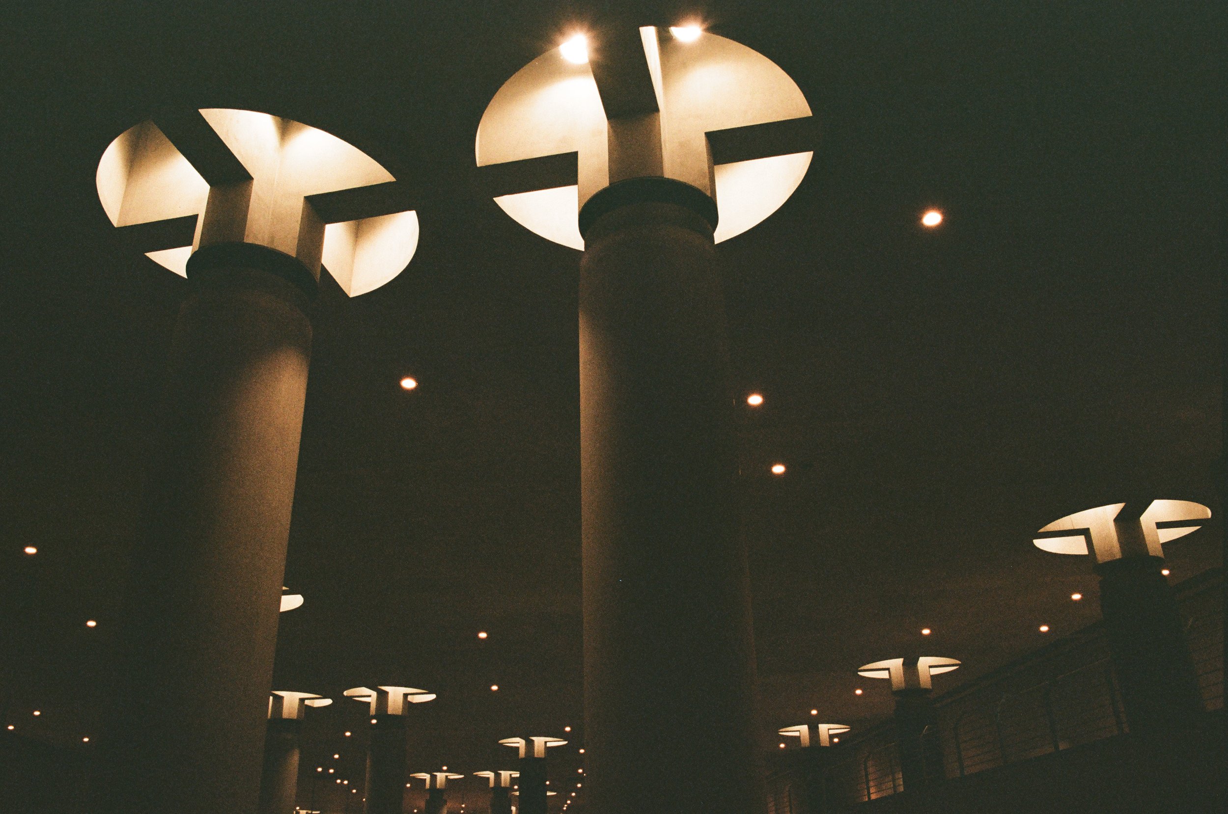 Der Blick nach oben auf große, runde Deckenlampen über mehreren Säulen in einem dunklen Raum.
