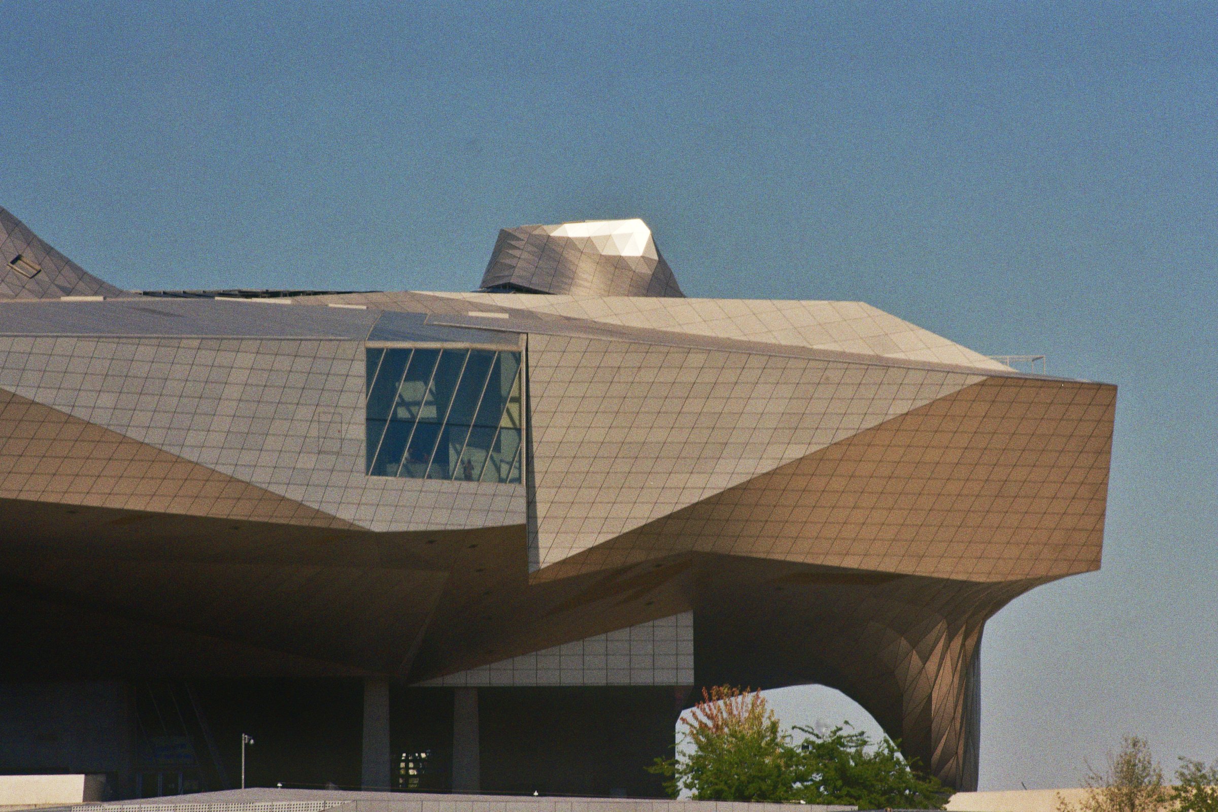 Moderne Architektur mit geometrischen Formen und reflektierendem Glas unter klarem blauen Himmel.