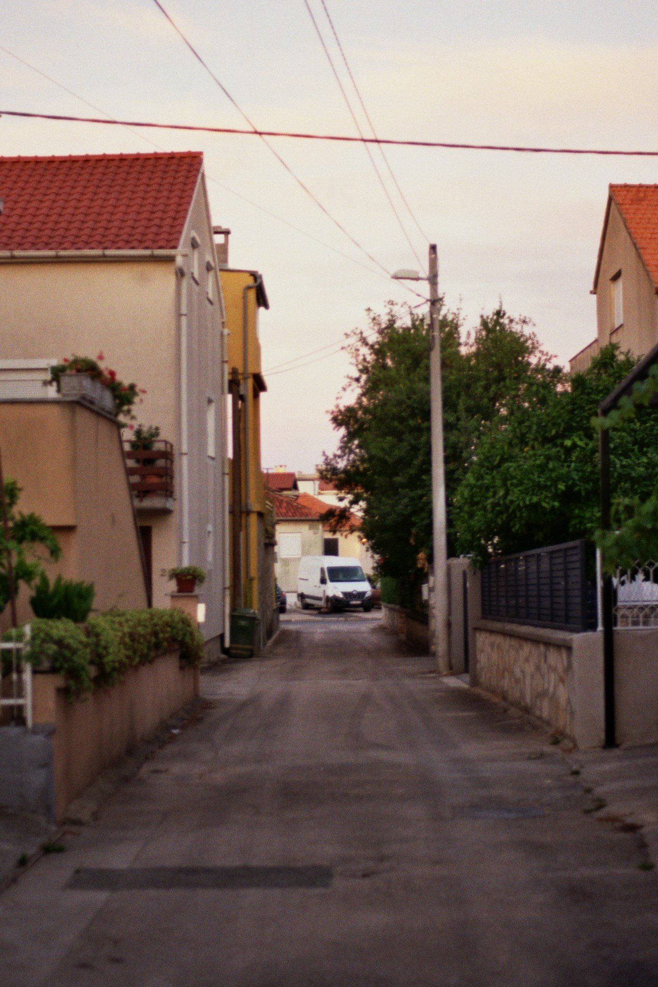 Eine ruhige, enge Straße in einem Wohnviertel mit Häusern auf beiden Seiten, einem weißen Lieferwagen im Hintergrund und sky mit dünnen Wolken.