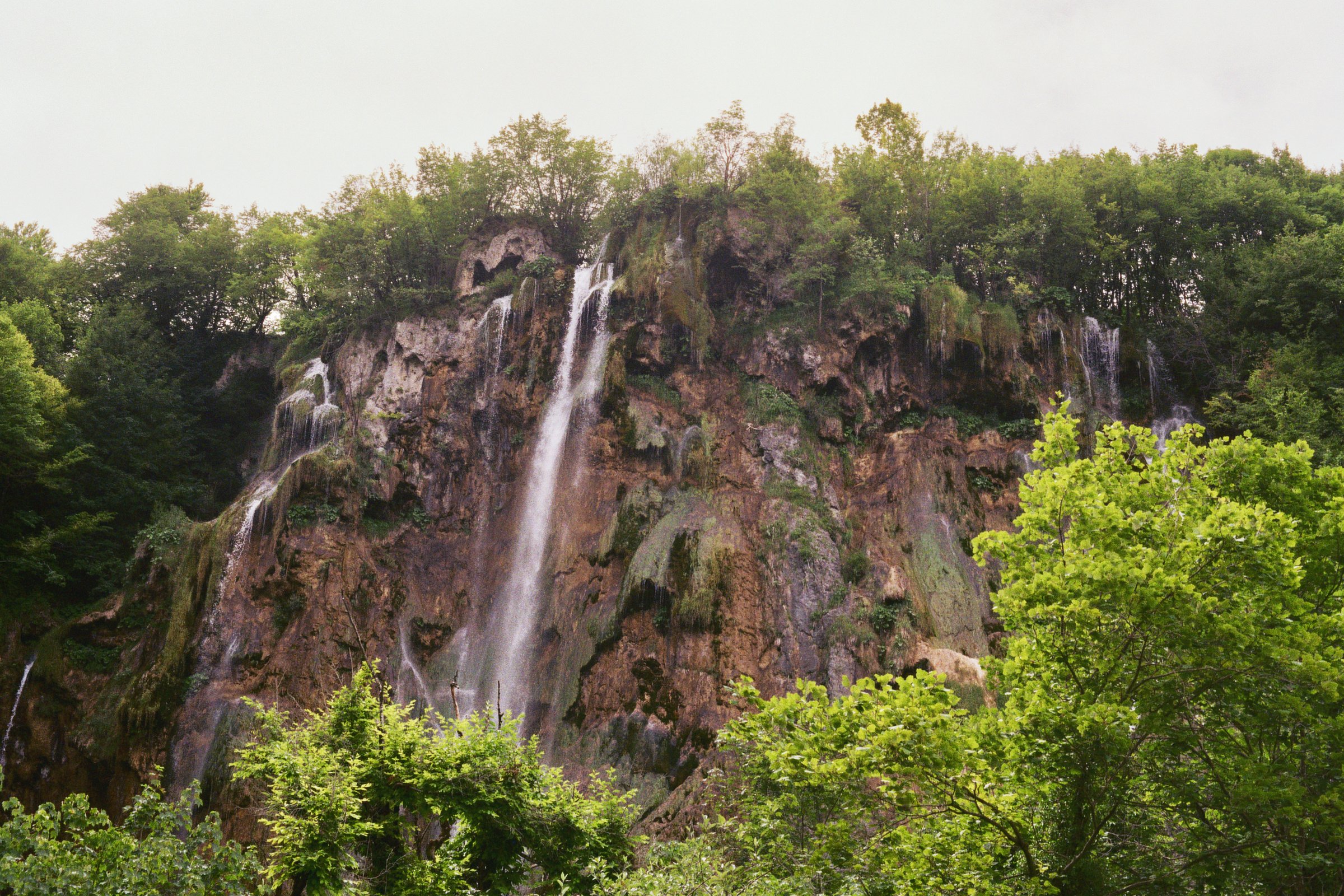 Wasserfall inmitten eines Waldes mit grünen Laubbäumen.