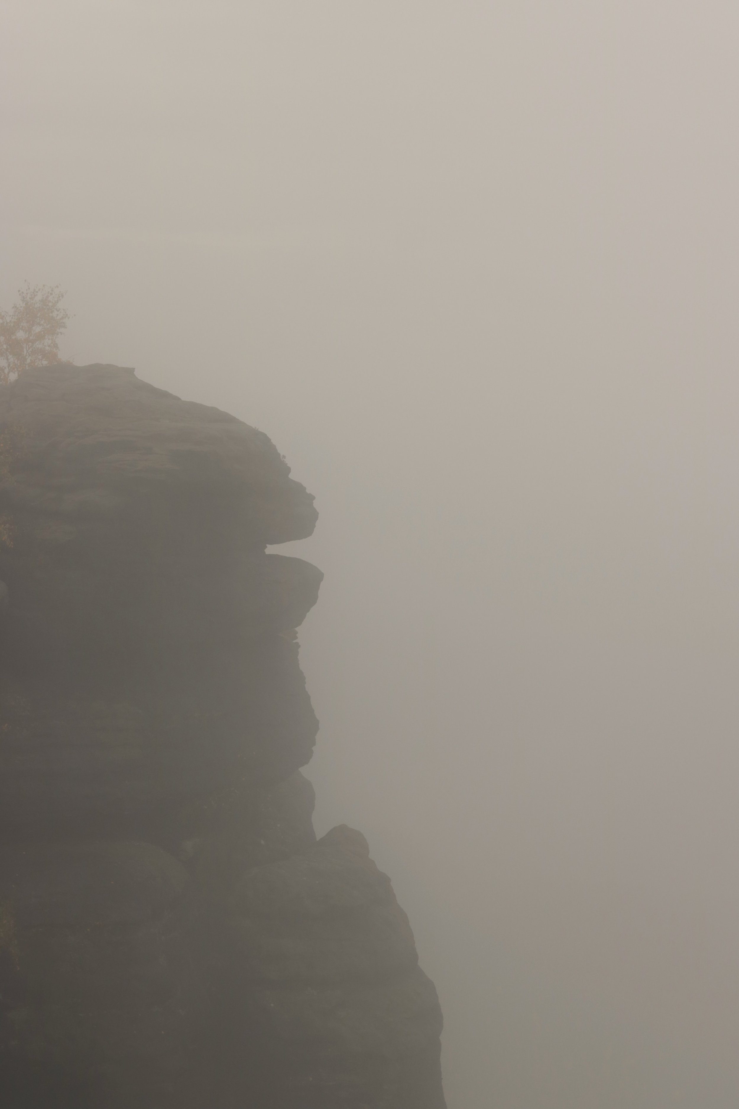 Felsformationen an einem nebligen See, reflektiert im Wasser.