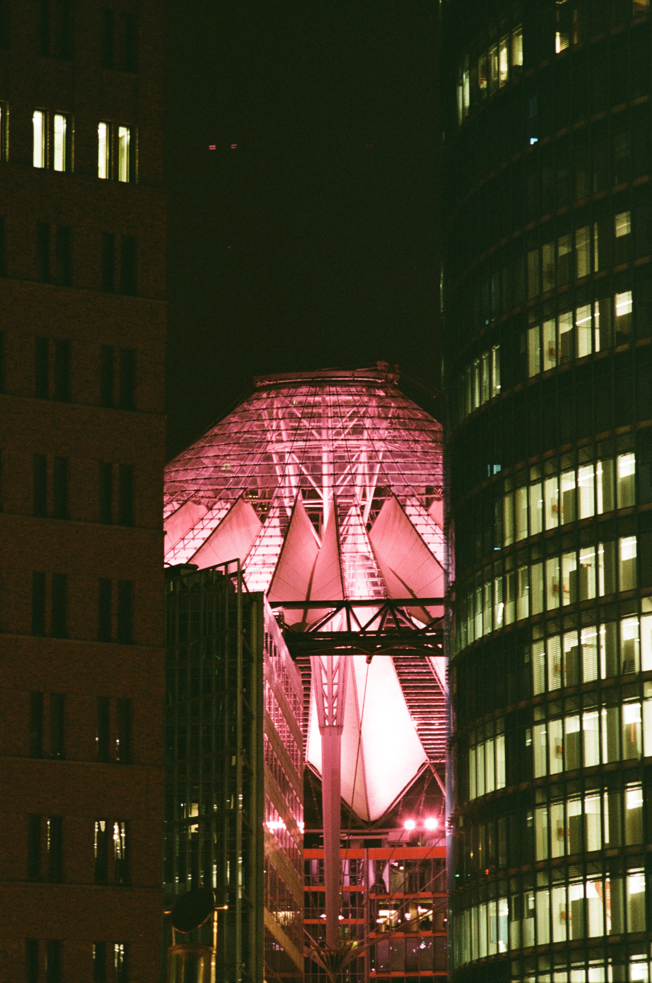 Ein moderner, leuchtender Gebäudekomplex bei Nacht mit einer kupferfarbenen, runden Kuppel in der Mitte, umgeben von Glas- und Betonstrukturen.