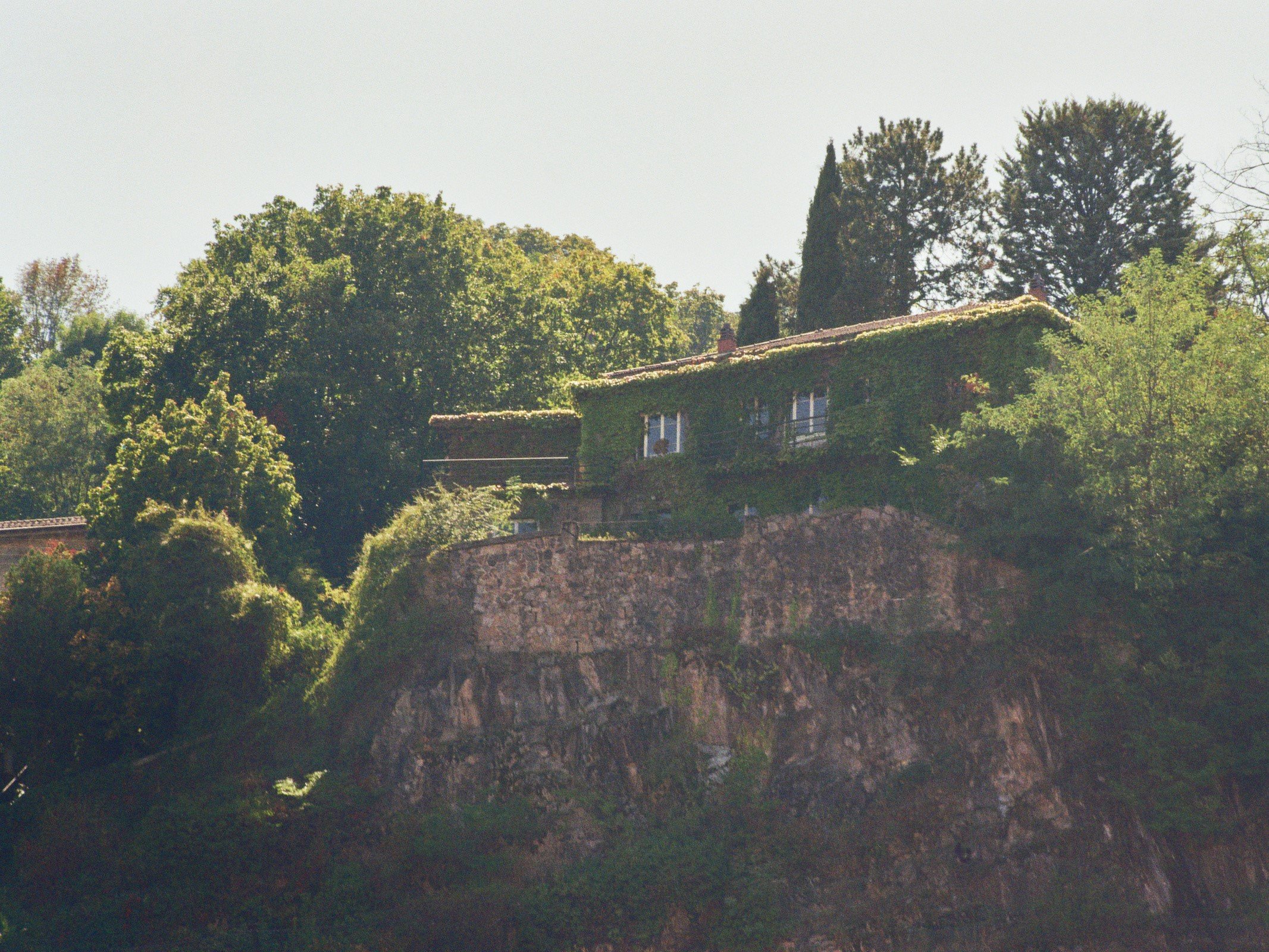 Ein Haus auf einer Klippe, umgeben von Bäumen, auf einem Felsen hoch oben an einem sonnigen Tag.