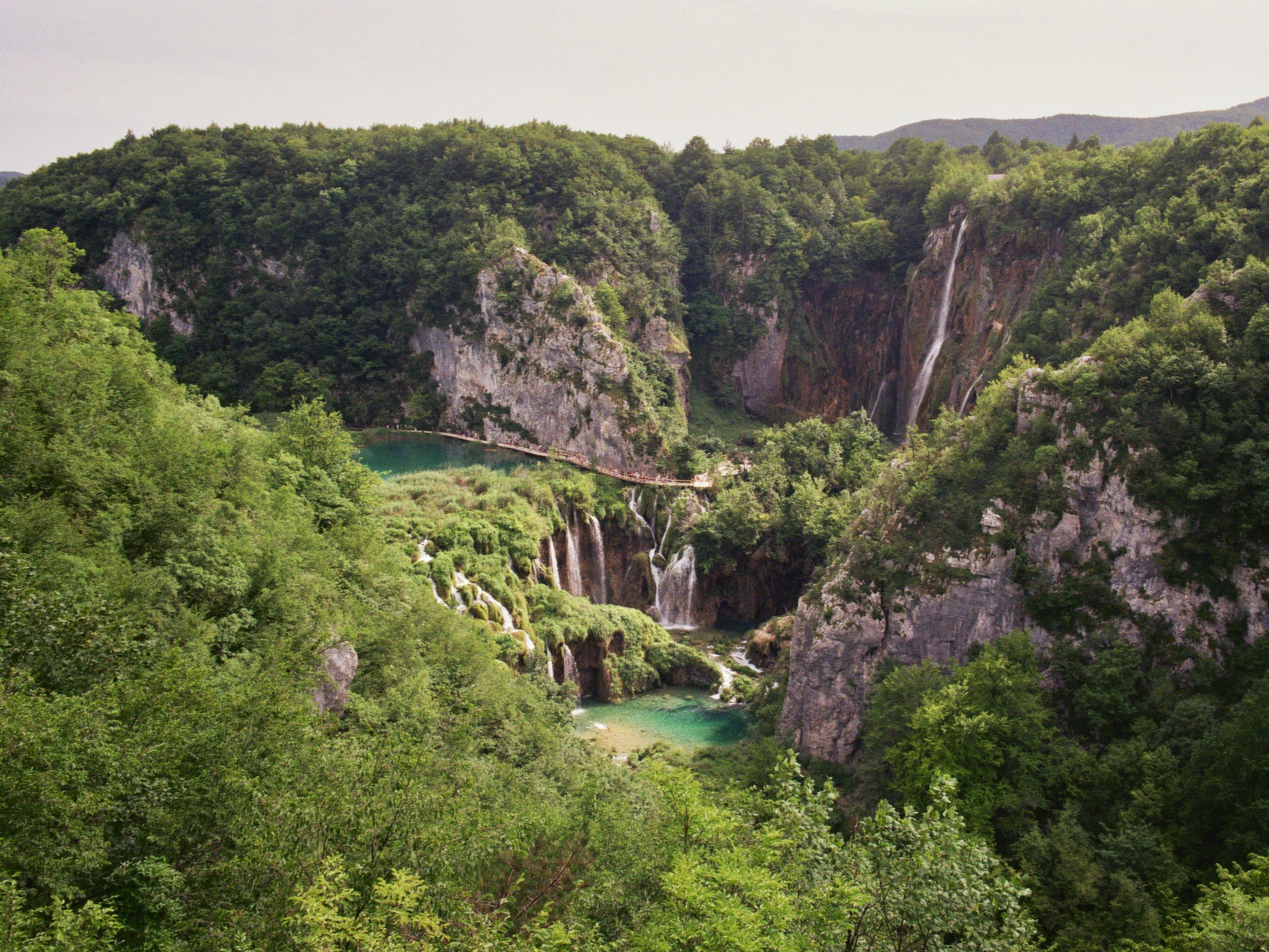Grüne Berge mit Wasserfällen, Wasser und Wald bei Tag, in der Nähe eines Sees.