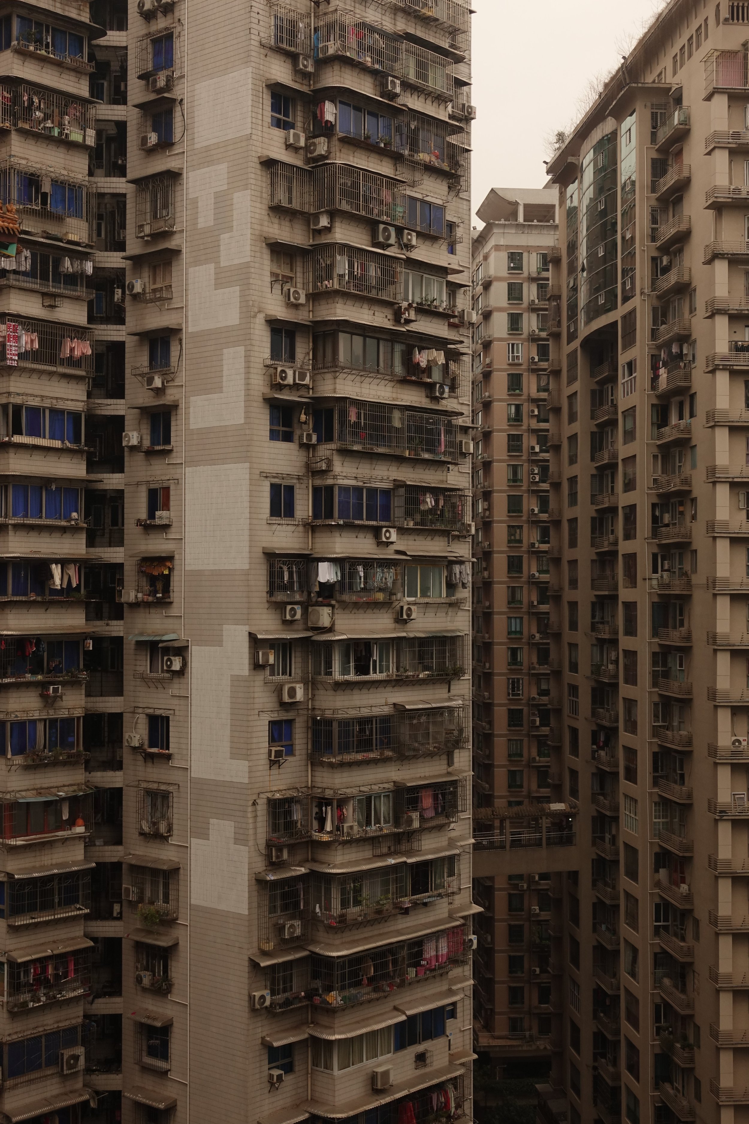 Hochhäuser in einer urbanen Siedlung mit Balkonen, an denen Kleidung und Gegenstände zum Trocknen oder Lagern hängen.