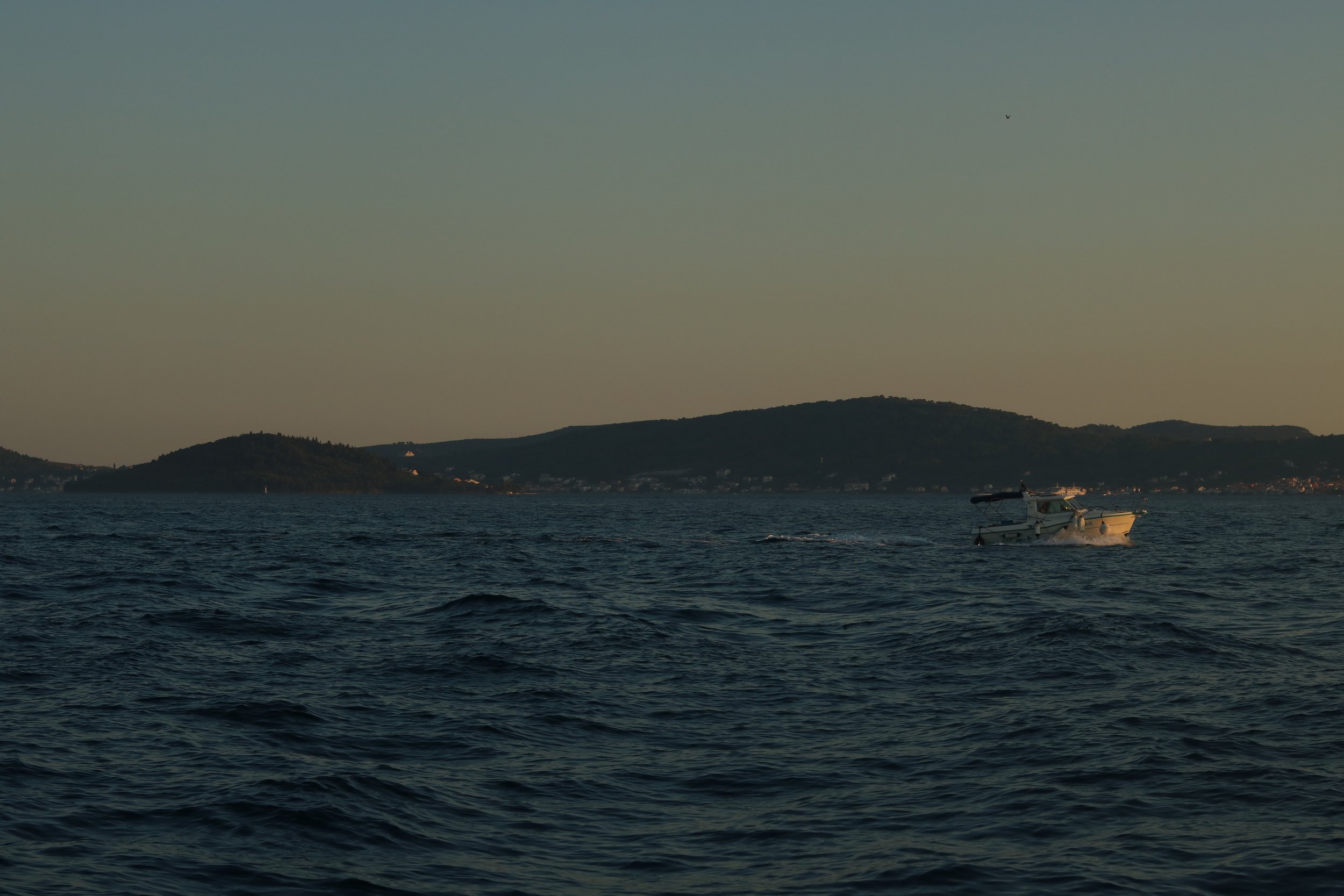 Ein Boot gleitet auf dem Wasser vor einer hügeligen Küstenlandschaft bei Sonnenuntergang.