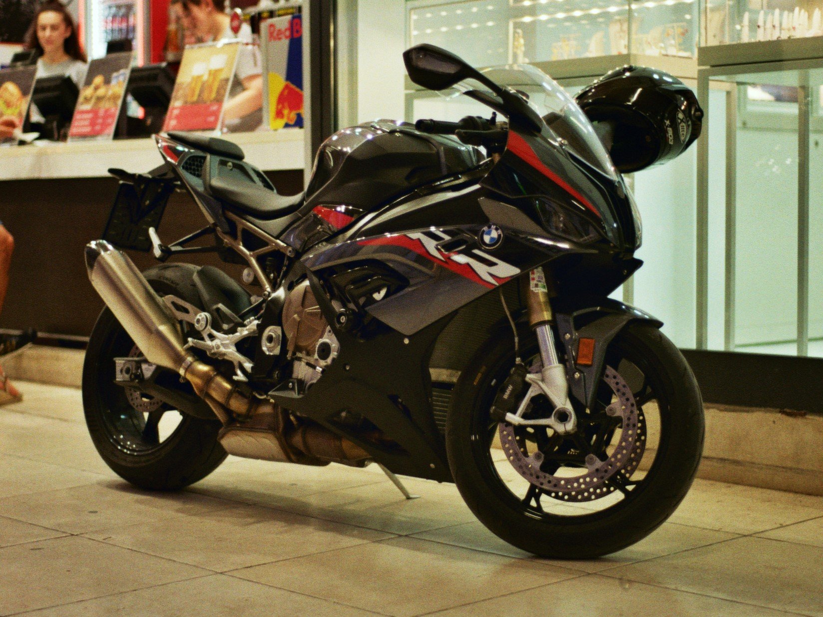 Ein schwarzes BMW Motorrad S1000RR Motorrad mit Helm, abgestellt vor einem Laden.