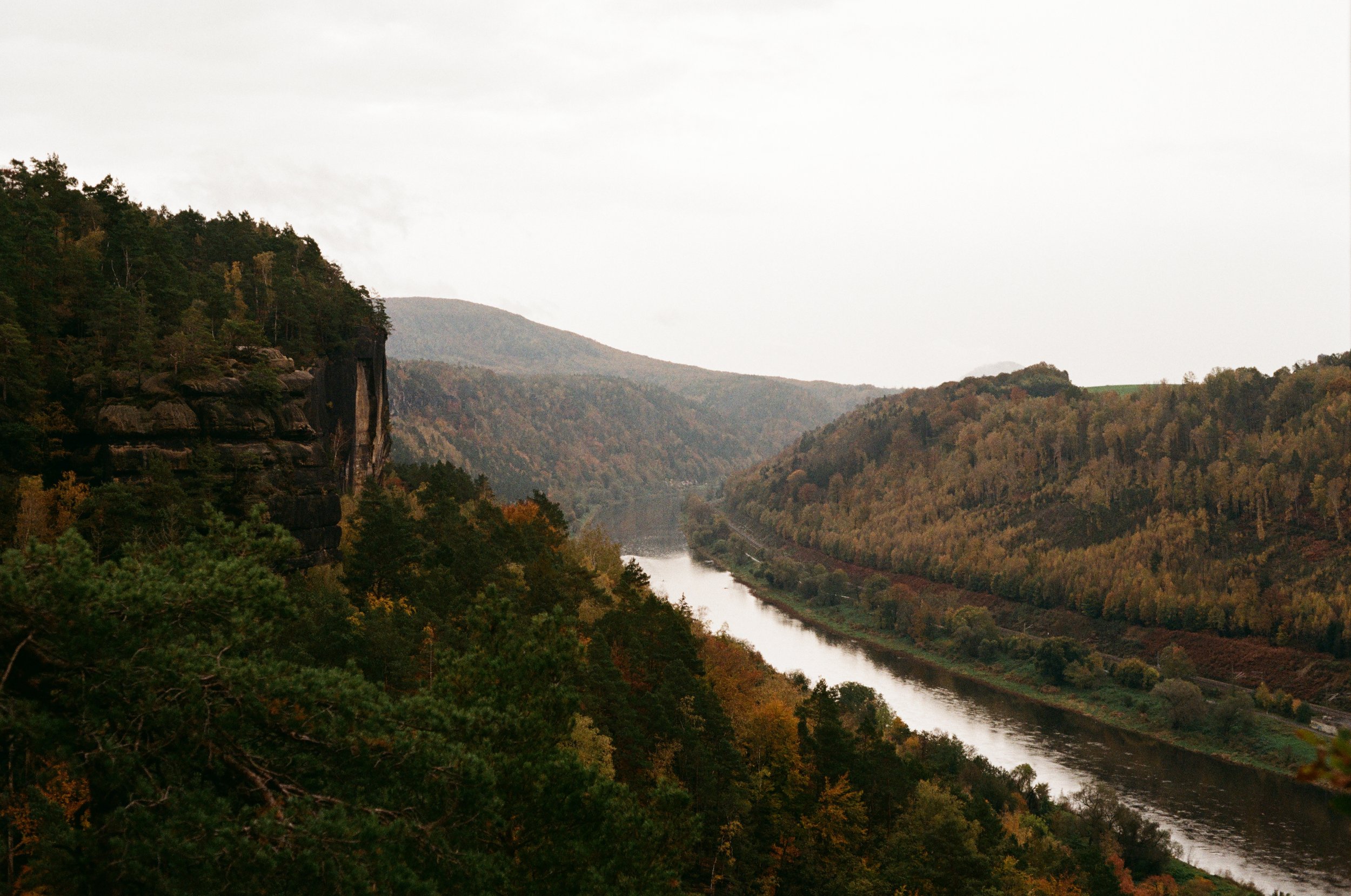 Fluss im Tal, umgeben von Hügeln und dichten Wäldern im Herbst