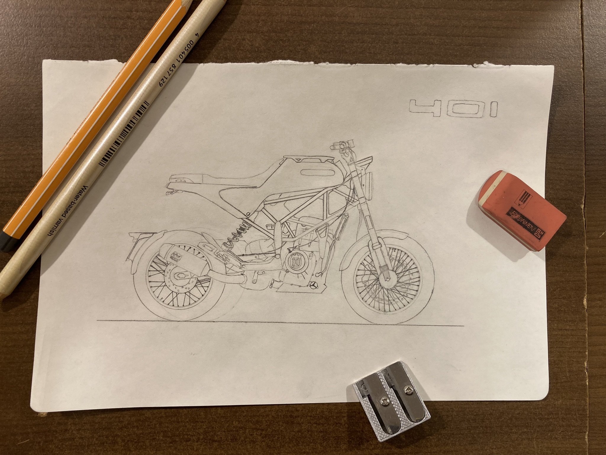Skizze eines Motorrads auf einem Blatt Papier, daneben ein Radiergummi, ein Lineal, ein Marker und zwei Bleistifte auf einem Holztisch.