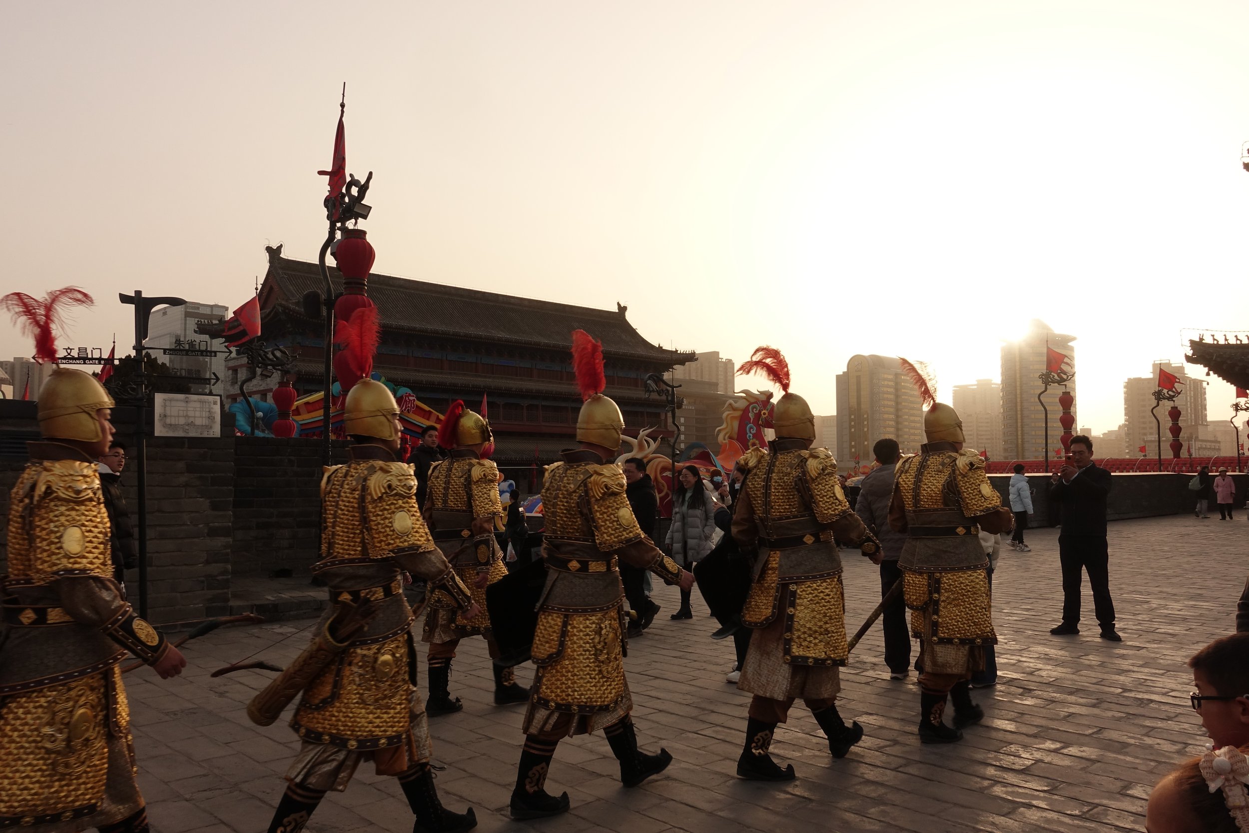 Menschen in goldenen Soldatenkostümen gehen in einer traditionellen Prozession vor einem chinesischen Tempel bei Sonnenuntergang.