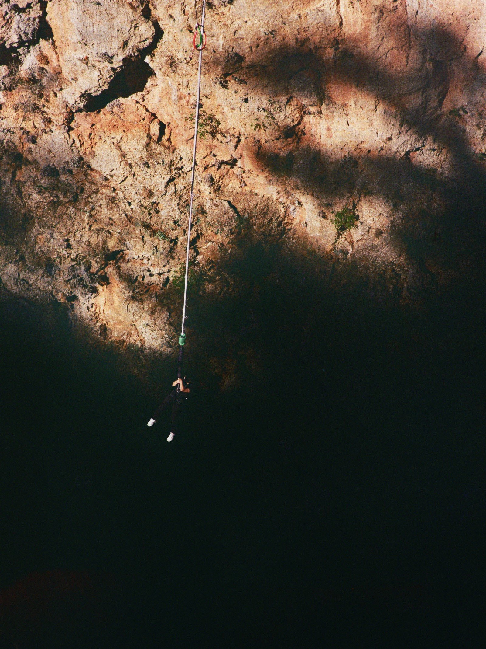 Eine Person hängt mit einem Seil an einer Felswand, die eine Höhle oder eine Schlucht bildet, im Dunkeln.