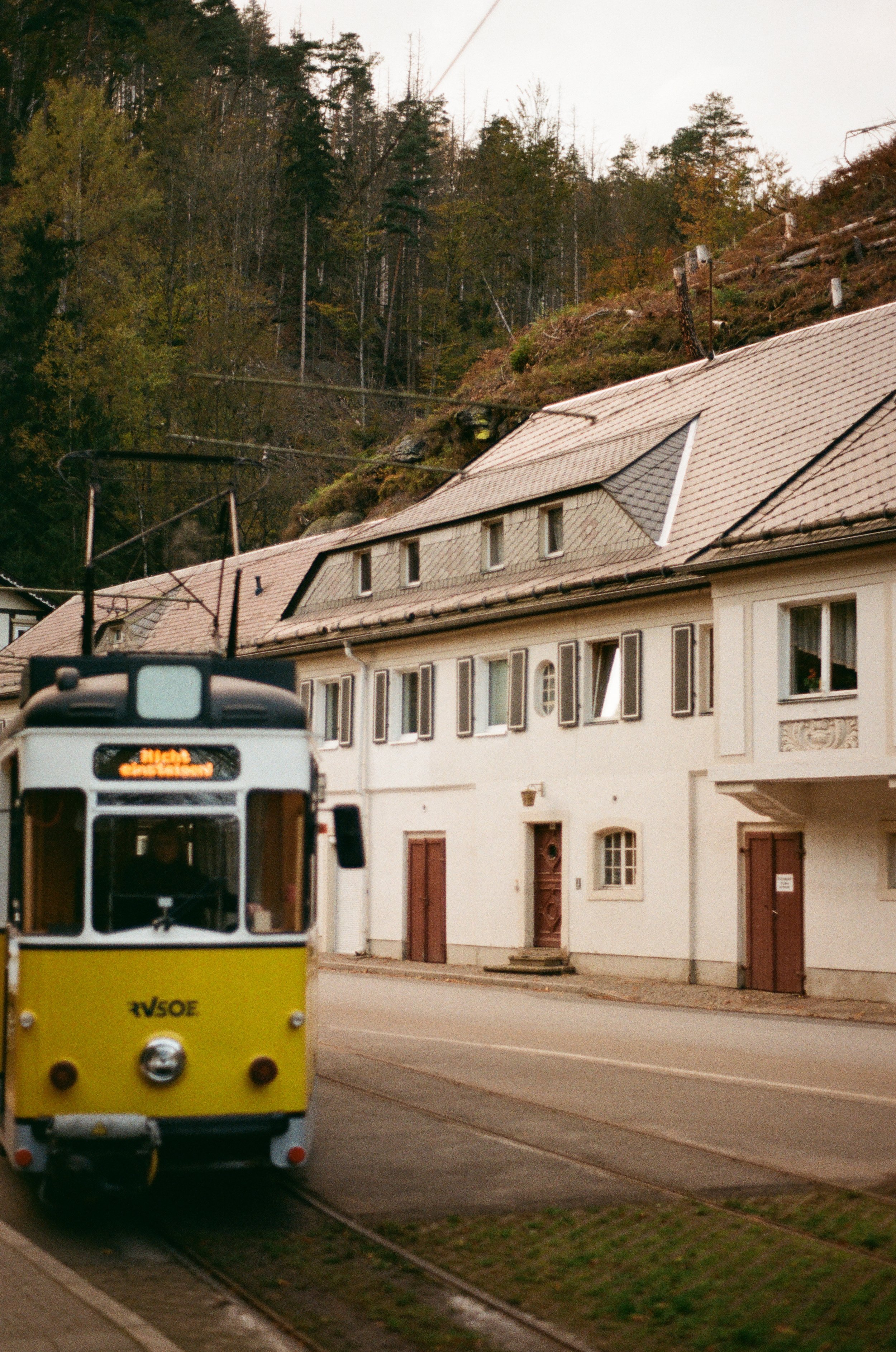 Straßenbahn fährt an einer weißen Hauswand in einer kleinen Stadt mit Hügeln im Hintergrund.