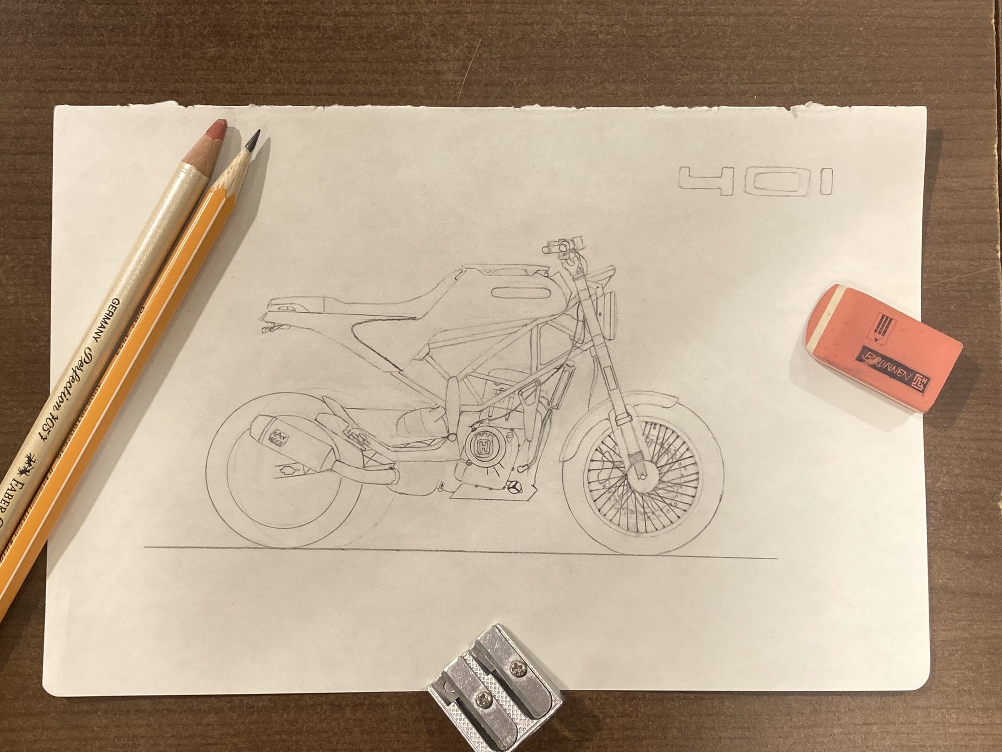 Skizze eines Motorrads auf einem weißen Blatt Papier, mit Bleistift und zwei Buntstiften, Radiergummi und Messer auf einem Holztisch
