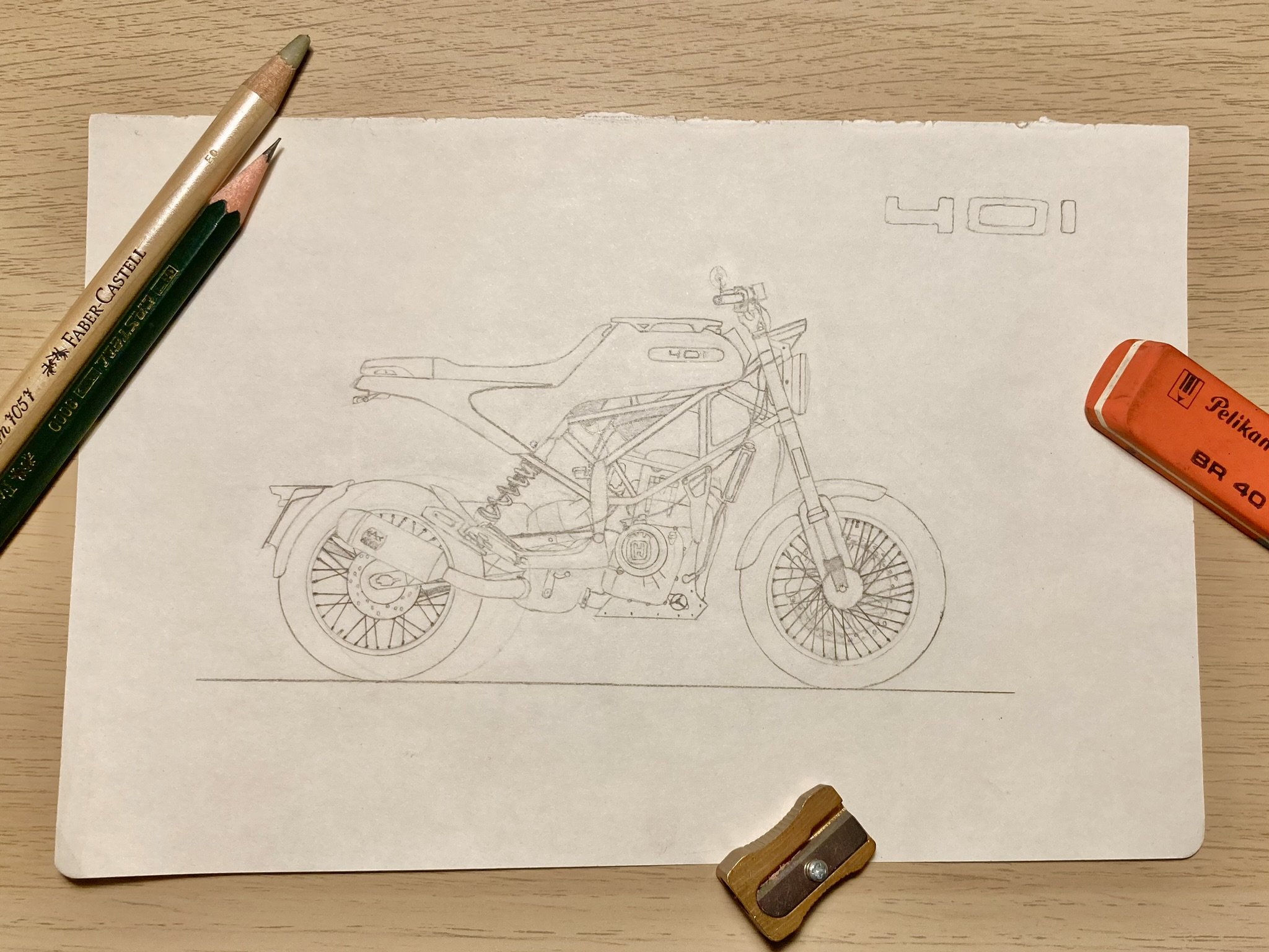 Skizze eines Motorrads auf einem Blatt Papier, umgeben von Bleistiften, einem Radiergummi und einem kleinen Messer.