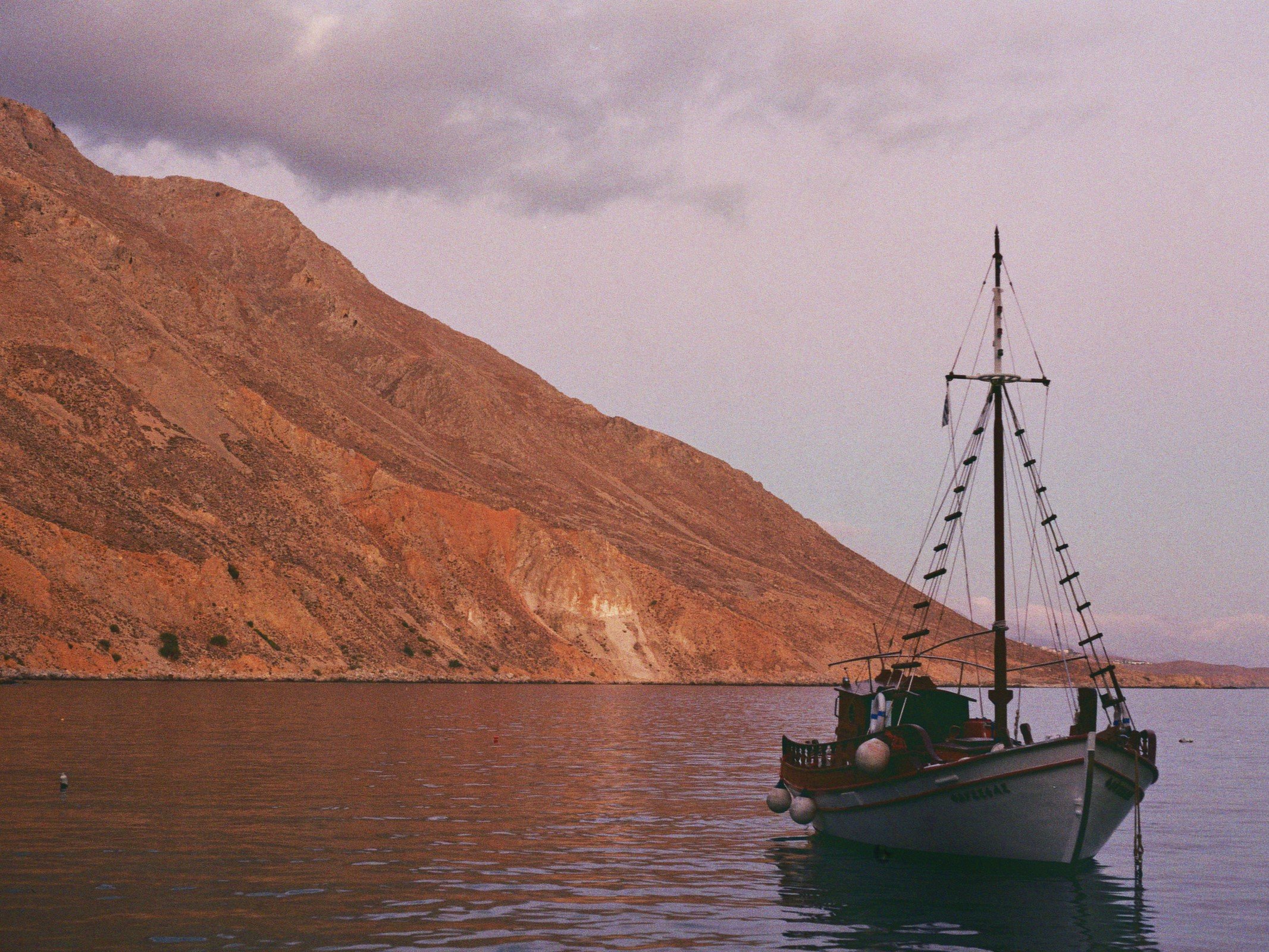 Ein Boot auf ruhigem Wasser vor einem felsigen Berg bei Sonnenuntergang, mit dunklen Wolken am Himmel.