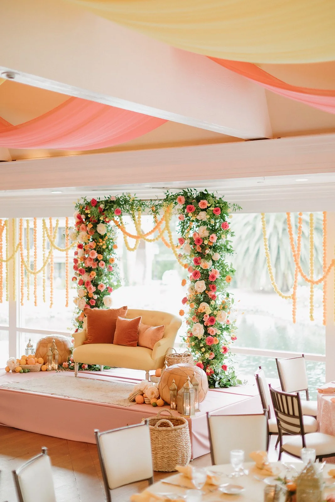 Elegant event space decorated with floral arch, pastel-colored drapes, and seating area with pillows.