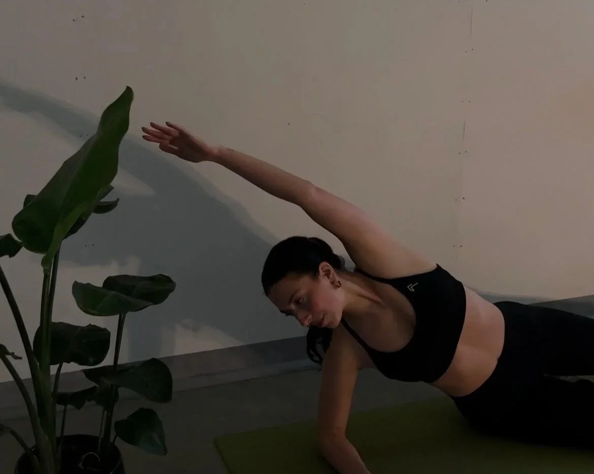 Woman practicing yoga side plank on mat indoors