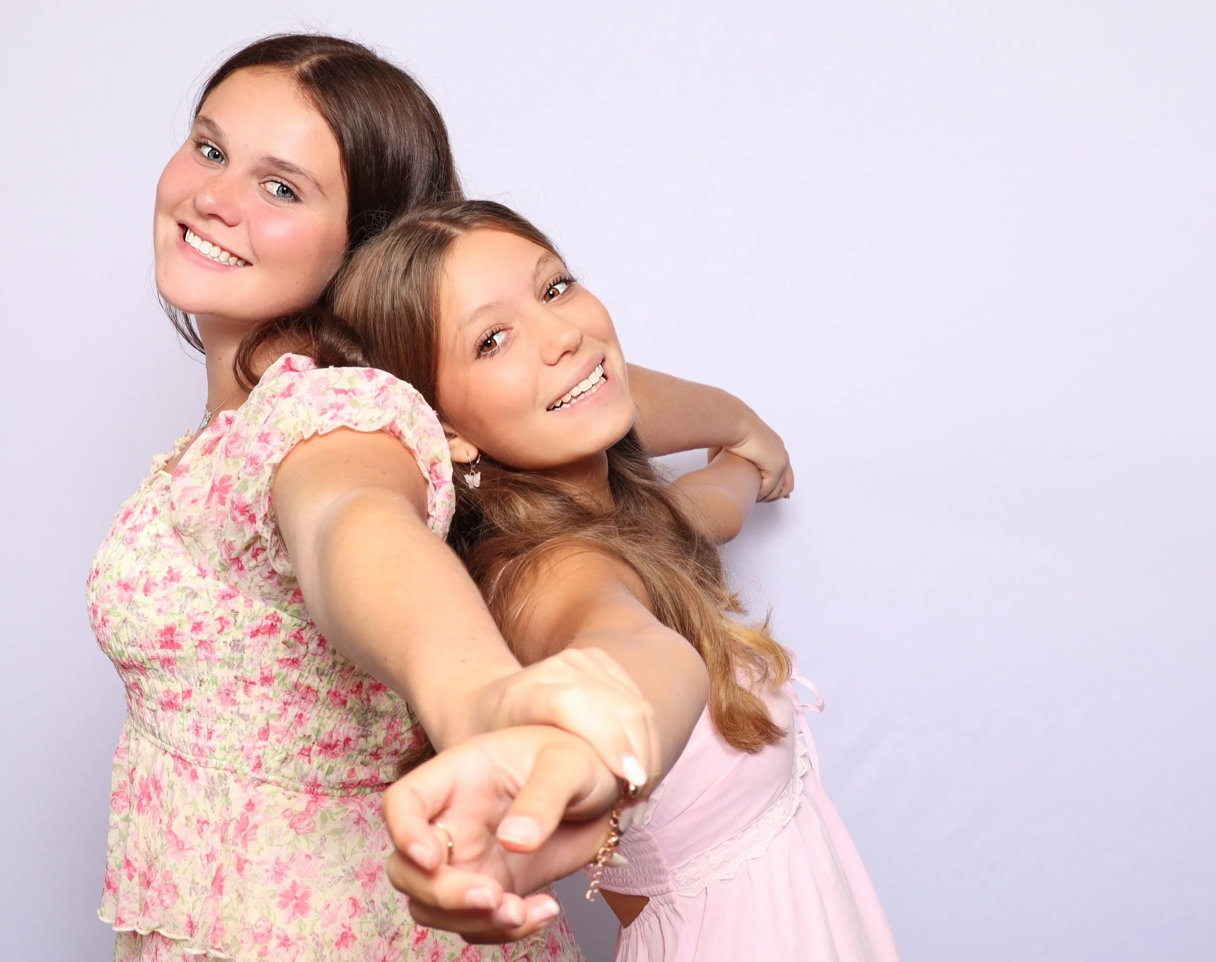 Two smiling women, one older and one younger, holding hands and taking a selfie together, against a plain light background.