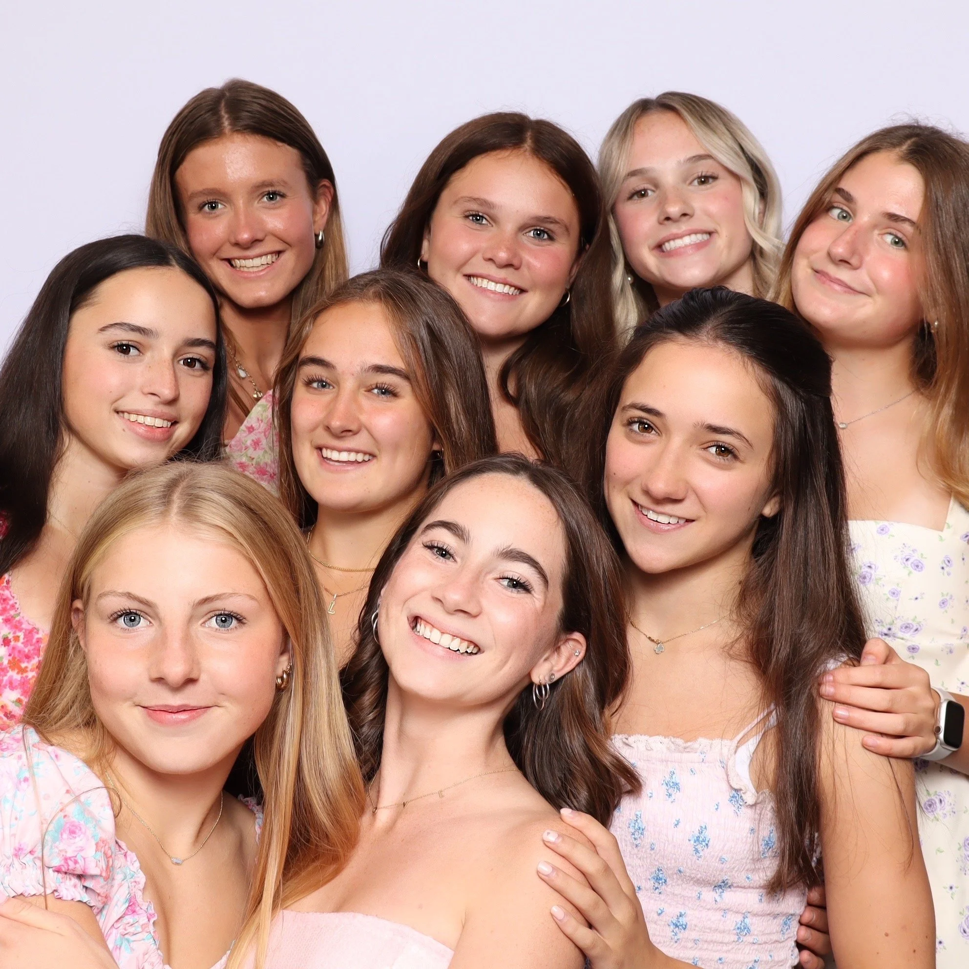 Group of ten young women smiling for a photo in a studio with a white background.