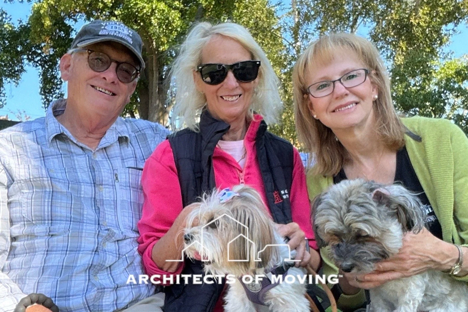 Three smiling people holding two small dogs outdoors with trees in the background, and a logo that reads 'Architects of Moving' at the bottom.